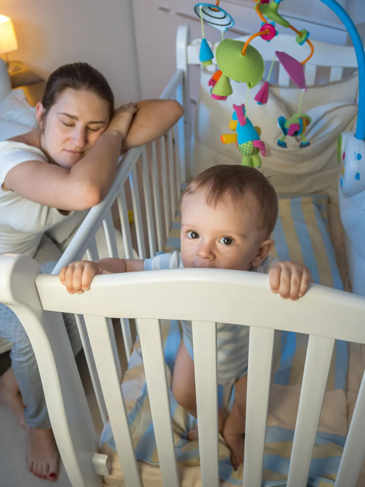 Young tired mother got asleep next to baby's crib