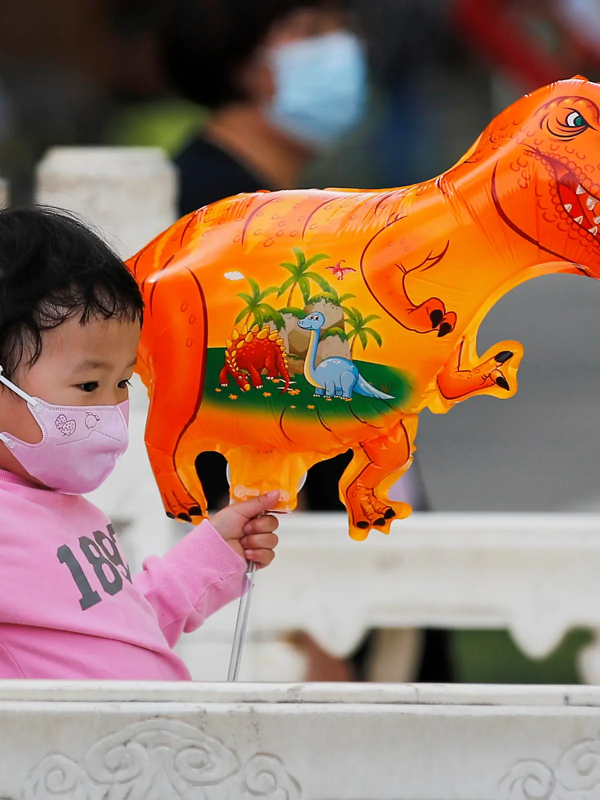A child wearing a face mask to help curb the spread of the coronavirus holds a dinosaur shaped balloon walks at a public park in Beijing, Sunday, May 16, 2021. (AP Photo/Andy Wong)