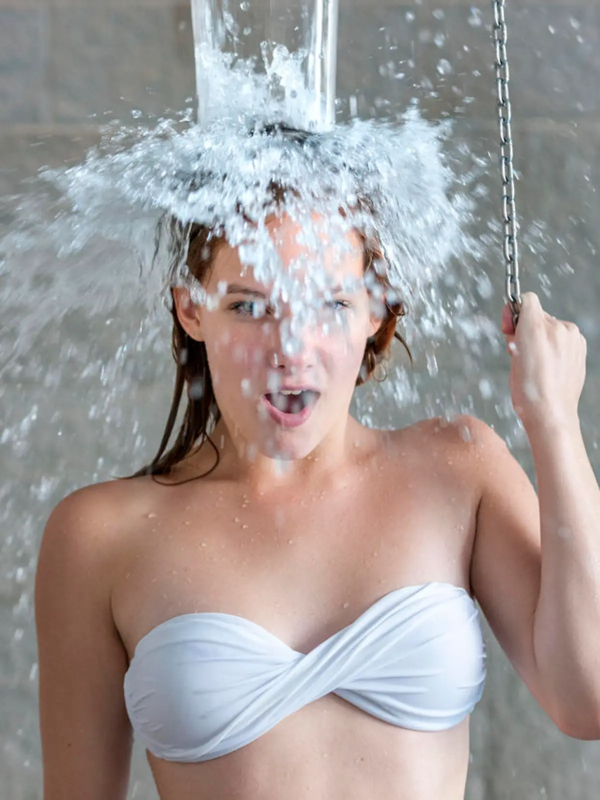 teenage girl gasping for breath taking cold water shower after sauna looking at the camera in health spa