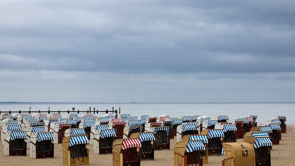 07.07.2022, Schleswig-Holstein, Travemünde: Nur wenige Menschen sind bei bedecktem Himmel zwischen den überwiegend geschlossenen Strandkörben an der Ostsee bei Travemünde unterwegs. Nach Schleswig-Holstein und Mecklenburg-Vorpommern haben am Donnerstag auch in Hamburg die Sommerferien begonnen. Foto: Christian Charisius/dpa +++ dpa-Bildfunk +++