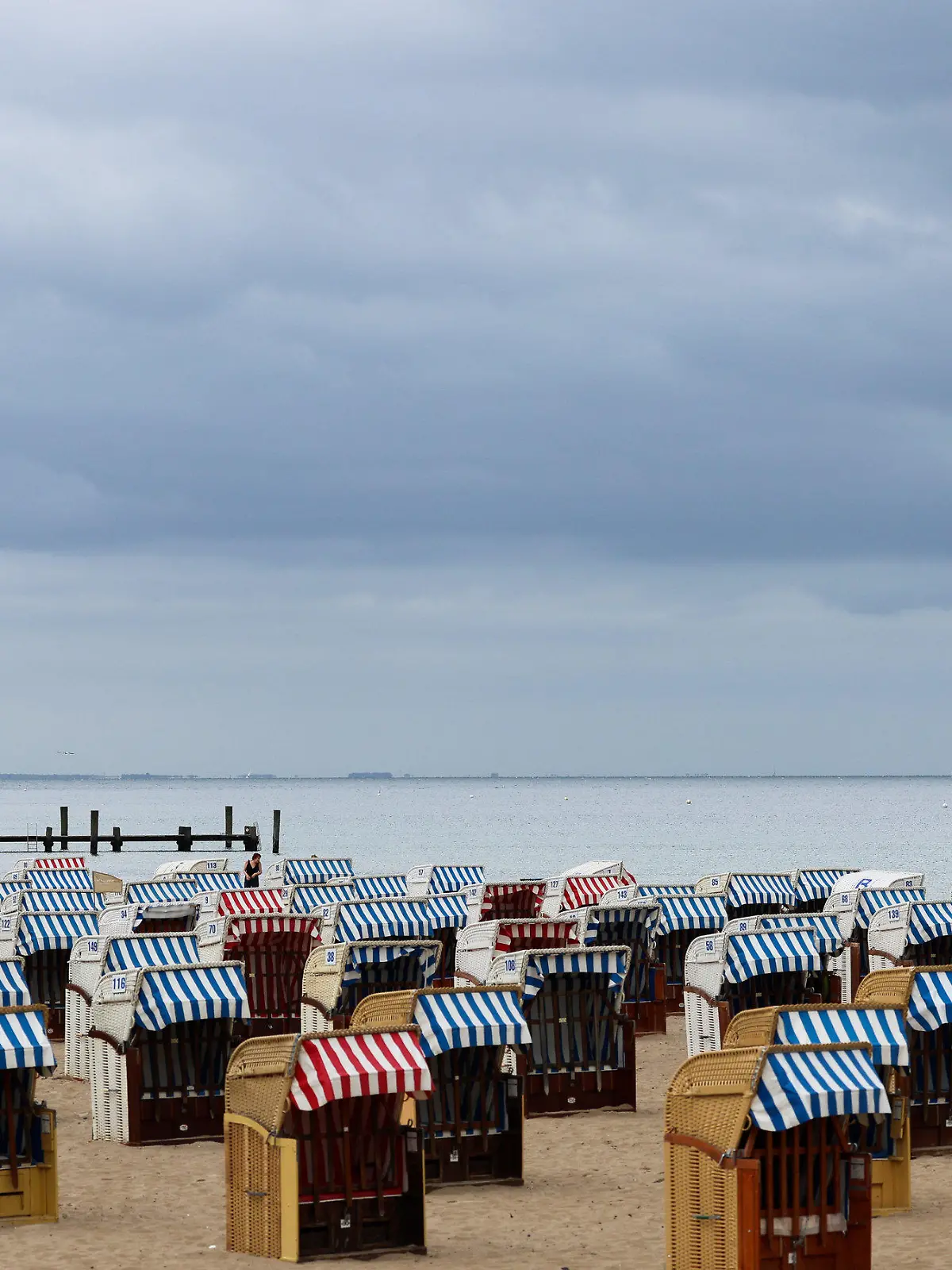 07.07.2022, Schleswig-Holstein, Travemünde: Nur wenige Menschen sind bei bedecktem Himmel zwischen den überwiegend geschlossenen Strandkörben an der Ostsee bei Travemünde unterwegs. Nach Schleswig-Holstein und Mecklenburg-Vorpommern haben am Donnerstag auch in Hamburg die Sommerferien begonnen. Foto: Christian Charisius/dpa +++ dpa-Bildfunk +++