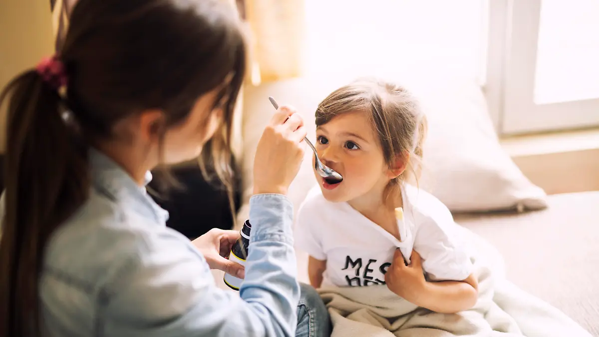 Mother giving daughter medicine on her sick daughter