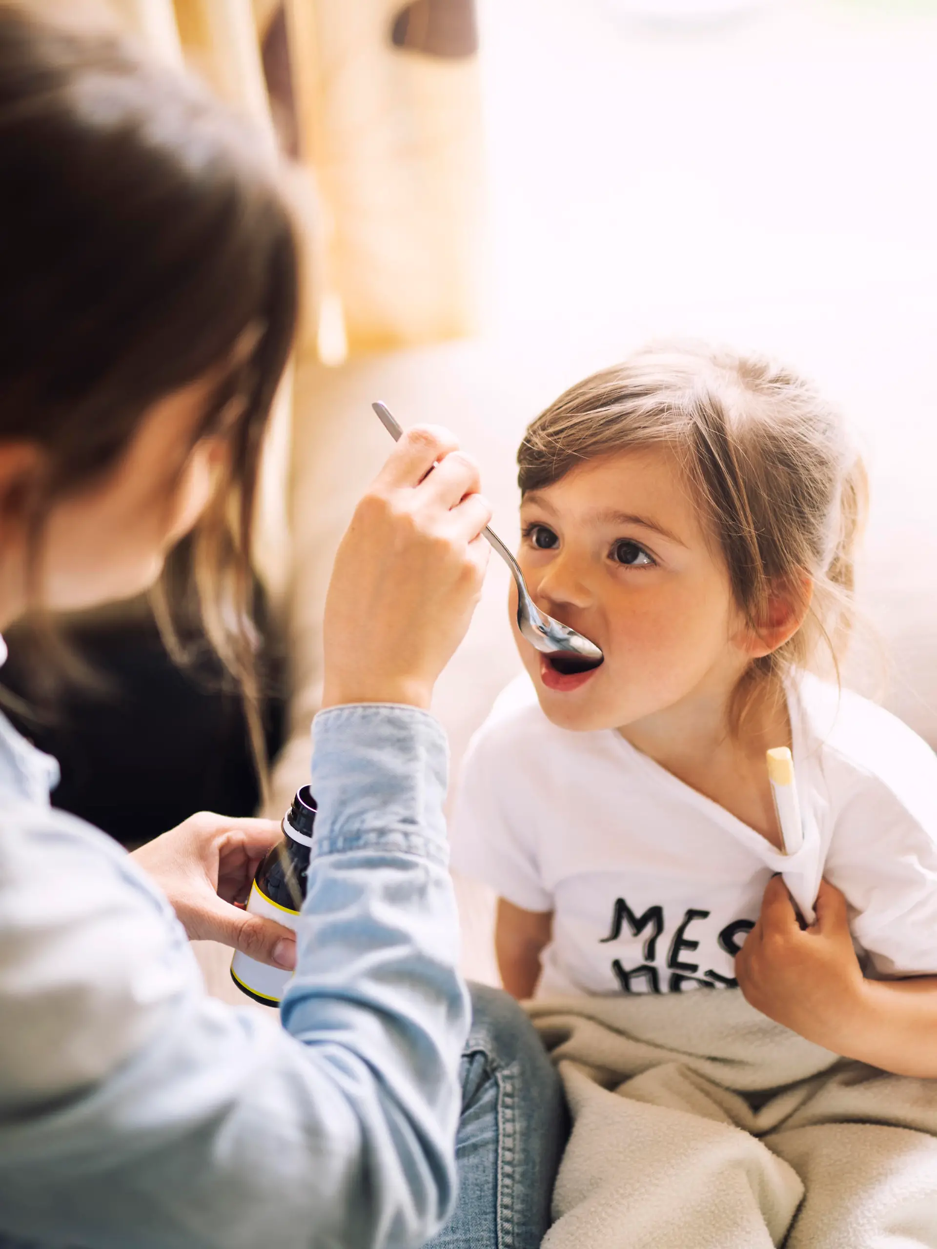 Mother giving daughter medicine on her sick daughter