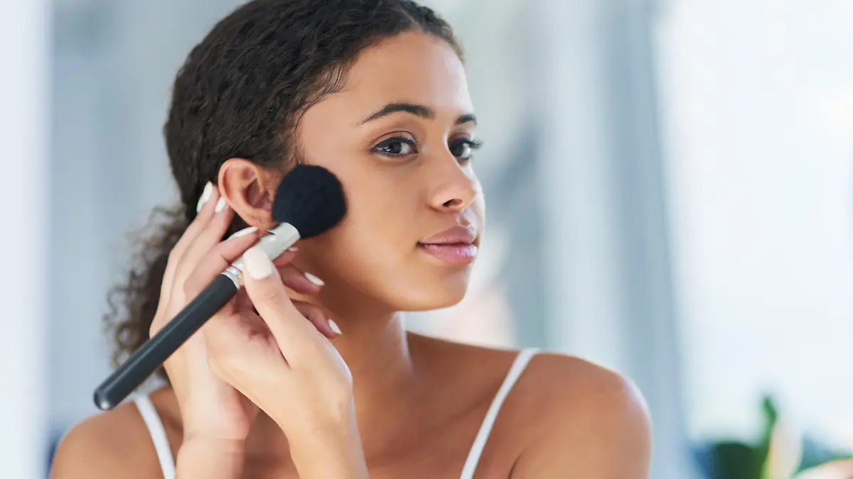 Cropped shot of a young woman applying makeup to her cheeks in the bathroom at home