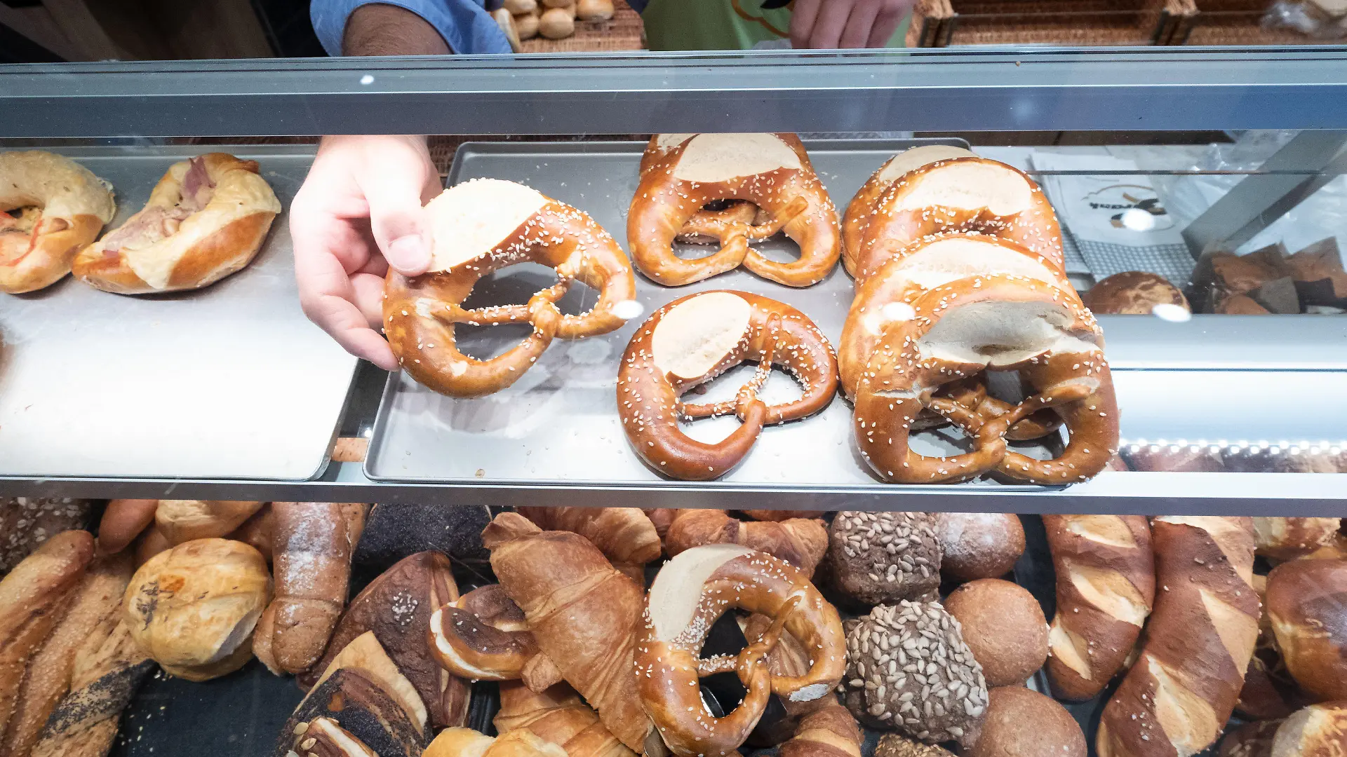 ARCHIV - 17.10.2019, Baden-Württemberg, Stuttgart: Ein Hand nimmt in einer Bäckerei eine Brezel aus einer Auslage. (zu dpa: «Gratisbrezeln für Pendler kosteten das Land fast 60 000 Euro») Foto: Bernd Weißbrod/dpa +++ dpa-Bildfunk +++