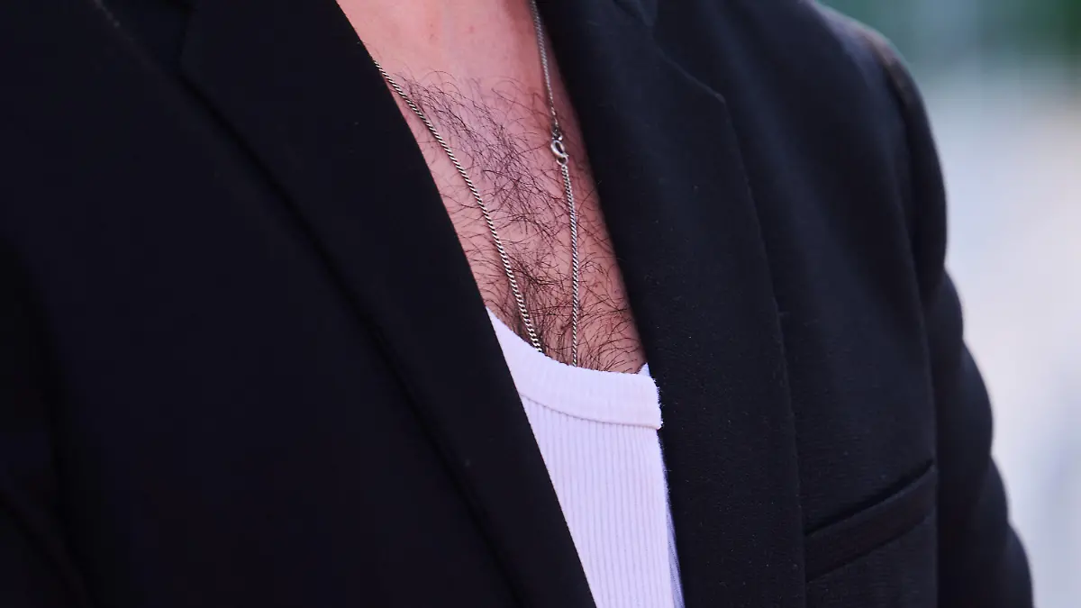 ILLUSTRATION - 24.06.2022, Berlin: Brusthaar ist bei einem Mann zu sehen, der ein weißes Rippenshirt zu einem Jacket trägt. (zu dpa-KORR Männer zum Kraulen - Gibt es ein Comeback der Brustbehaarung?) Foto: Annette Riedl/dpa +++ dpa-Bildfunk +++