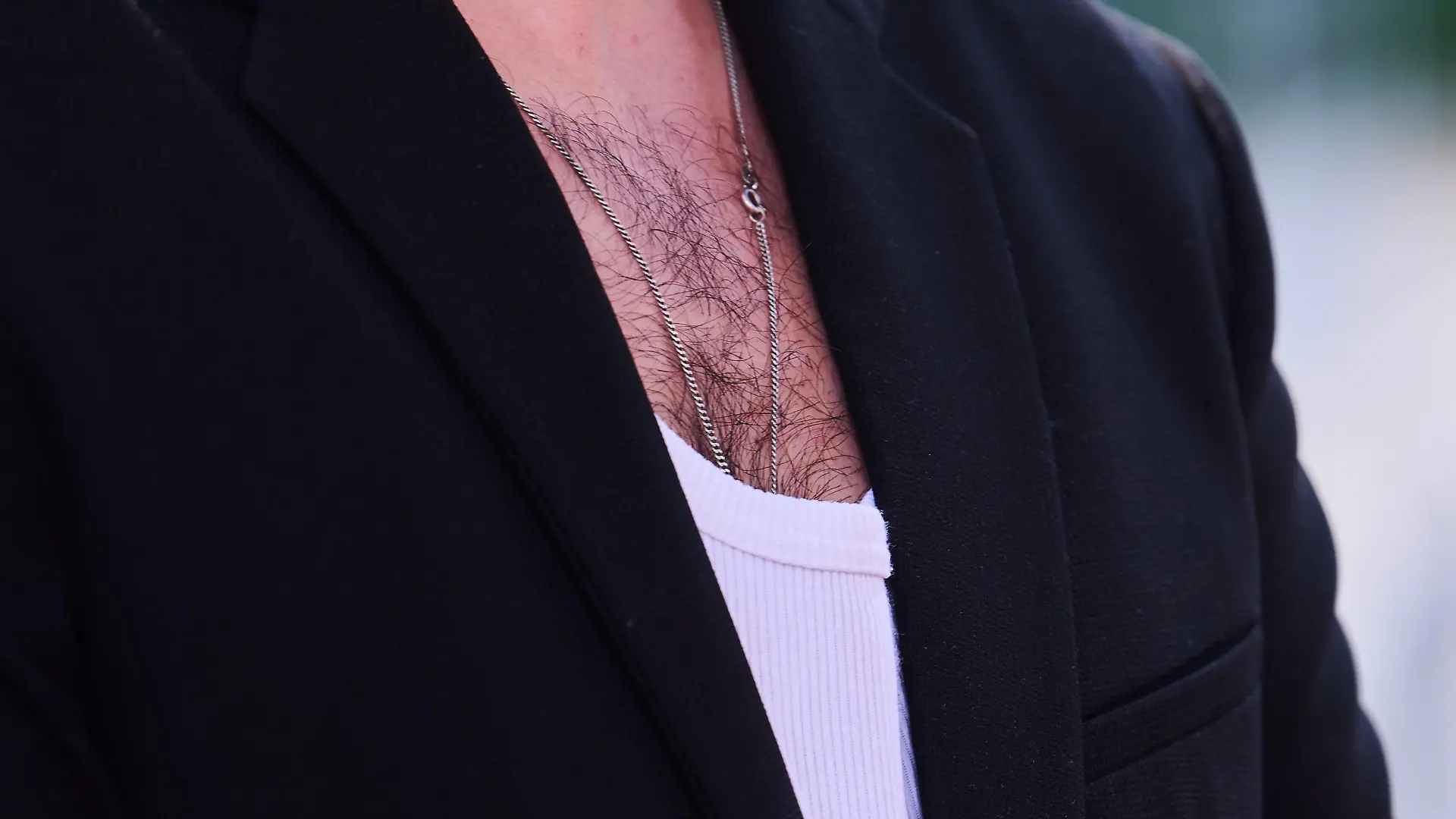 ILLUSTRATION - 24.06.2022, Berlin: Brusthaar ist bei einem Mann zu sehen, der ein weißes Rippenshirt zu einem Jacket trägt. (zu dpa-KORR Männer zum Kraulen - Gibt es ein Comeback der Brustbehaarung?) Foto: Annette Riedl/dpa +++ dpa-Bildfunk +++