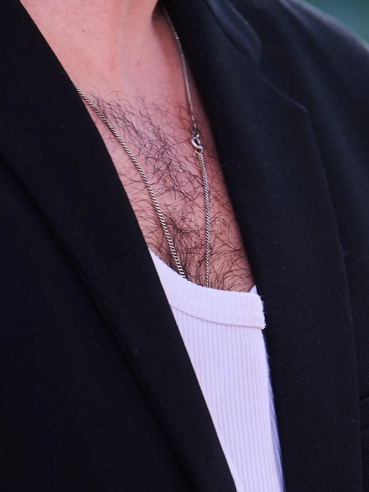 ILLUSTRATION - 24.06.2022, Berlin: Brusthaar ist bei einem Mann zu sehen, der ein weißes Rippenshirt zu einem Jacket trägt. (zu dpa-KORR Männer zum Kraulen - Gibt es ein Comeback der Brustbehaarung?) Foto: Annette Riedl/dpa +++ dpa-Bildfunk +++