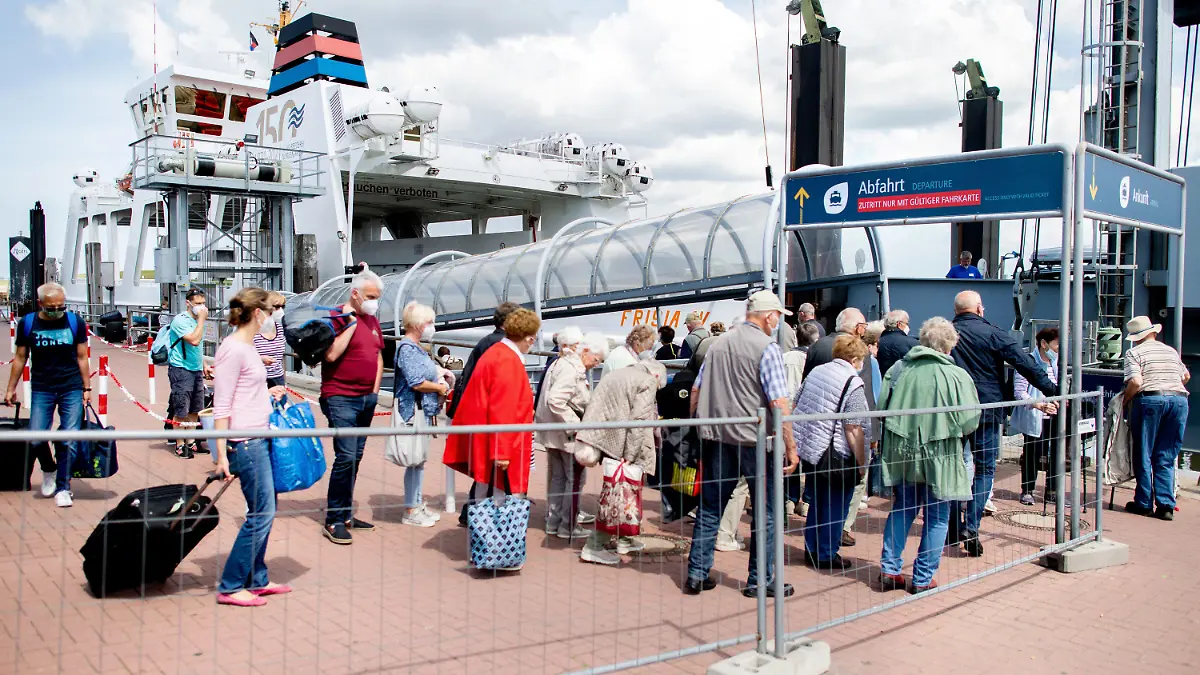 25.06.2022, Niedersachsen, Norddeich: Touristen warten mit ihrem Gepäck am Fährterminal im Hafen, um mit einem Fährschiff der AG Reederei Norden-Frisia auf die Insel Norderney zu fahren. Als erstes deutsches Bundesland ist Nordrhein-Westfalen in die Sommerferien gestartet. Foto: Hauke-Christian Dittrich/dpa +++ dpa-Bildfunk +++