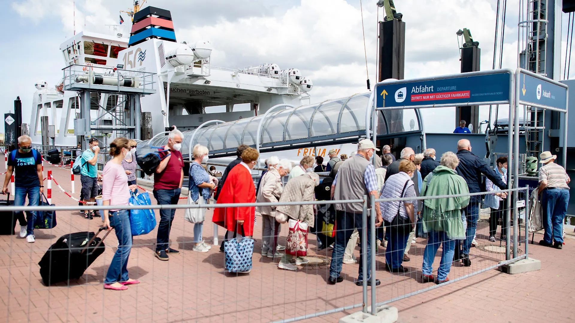 25.06.2022, Niedersachsen, Norddeich: Touristen warten mit ihrem Gepäck am Fährterminal im Hafen, um mit einem Fährschiff der AG Reederei Norden-Frisia auf die Insel Norderney zu fahren. Als erstes deutsches Bundesland ist Nordrhein-Westfalen in die Sommerferien gestartet. Foto: Hauke-Christian Dittrich/dpa +++ dpa-Bildfunk +++