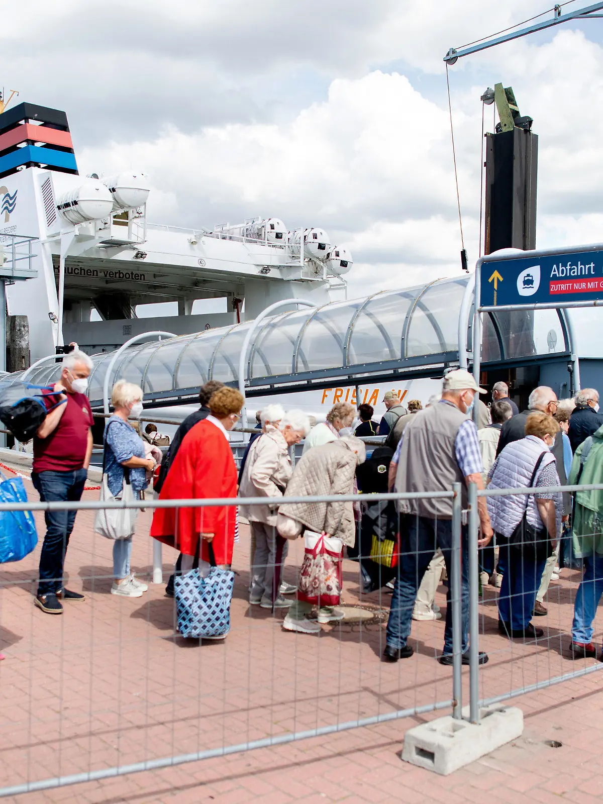 25.06.2022, Niedersachsen, Norddeich: Touristen warten mit ihrem Gepäck am Fährterminal im Hafen, um mit einem Fährschiff der AG Reederei Norden-Frisia auf die Insel Norderney zu fahren. Als erstes deutsches Bundesland ist Nordrhein-Westfalen in die Sommerferien gestartet. Foto: Hauke-Christian Dittrich/dpa +++ dpa-Bildfunk +++