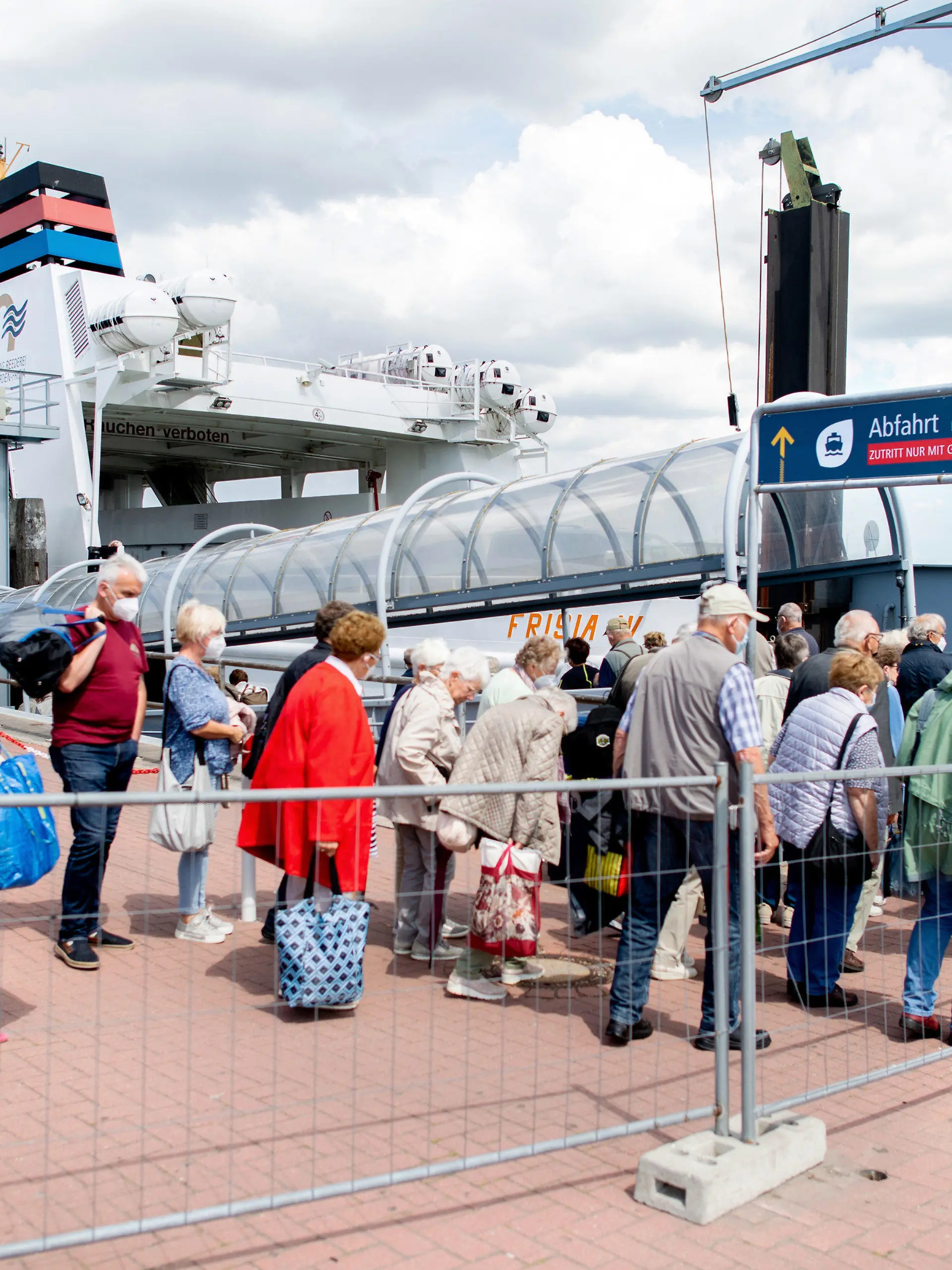 25.06.2022, Niedersachsen, Norddeich: Touristen warten mit ihrem Gepäck am Fährterminal im Hafen, um mit einem Fährschiff der AG Reederei Norden-Frisia auf die Insel Norderney zu fahren. Als erstes deutsches Bundesland ist Nordrhein-Westfalen in die Sommerferien gestartet. Foto: Hauke-Christian Dittrich/dpa +++ dpa-Bildfunk +++