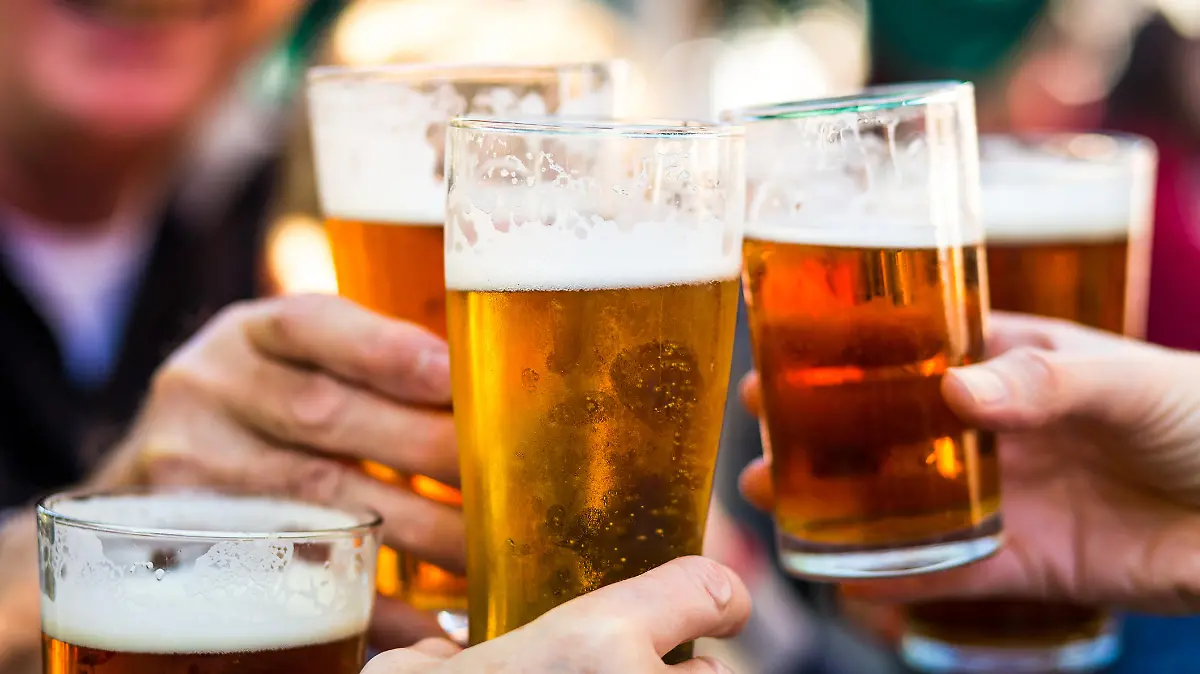 Close up color image depicting a group of people celebrating with a toast. The people cheers their glasses of beer (pints of beer) together in a gesture of celebration, togetherness and happiness. The people are defocused in the background, while focus is on the glasses of beer in the foreground. Room for copy space.