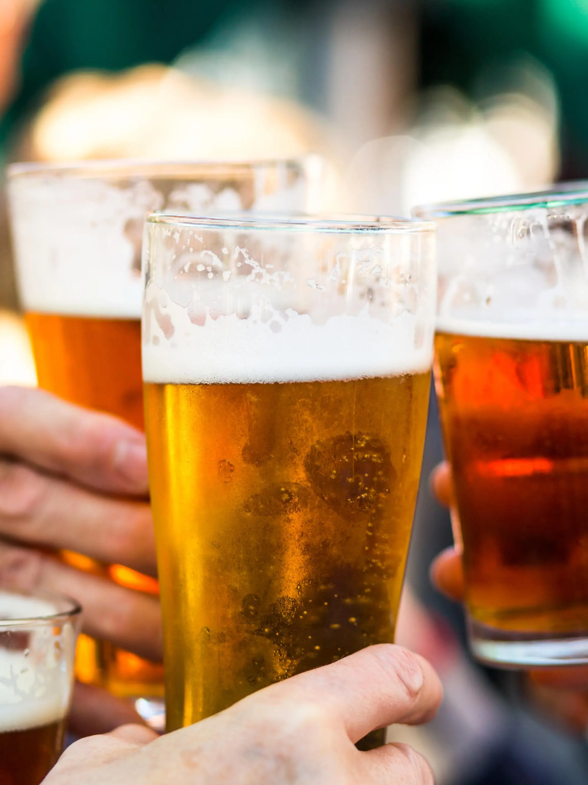 Close up color image depicting a group of people celebrating with a toast. The people cheers their glasses of beer (pints of beer) together in a gesture of celebration, togetherness and happiness. The people are defocused in the background, while focus is on the glasses of beer in the foreground. Room for copy space.