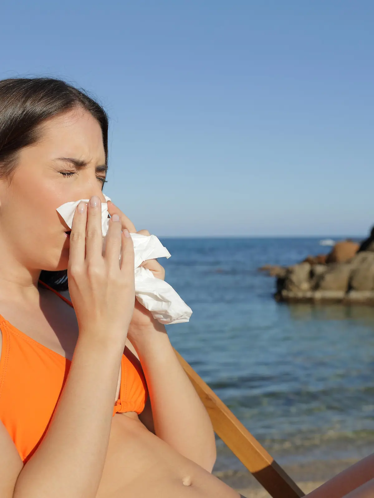 Sick tourist blowing nose with tissue on beach
