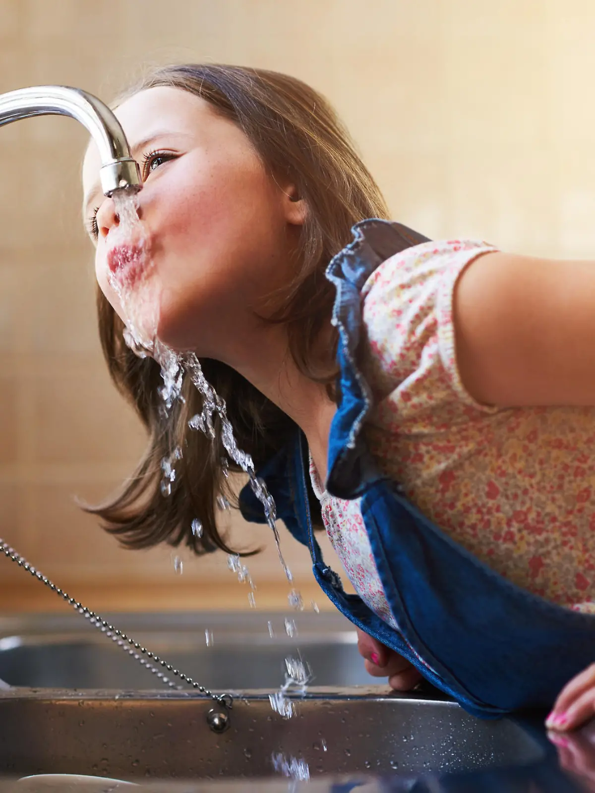 Shot of a little girl drinking water directly from the kitchen tap at home