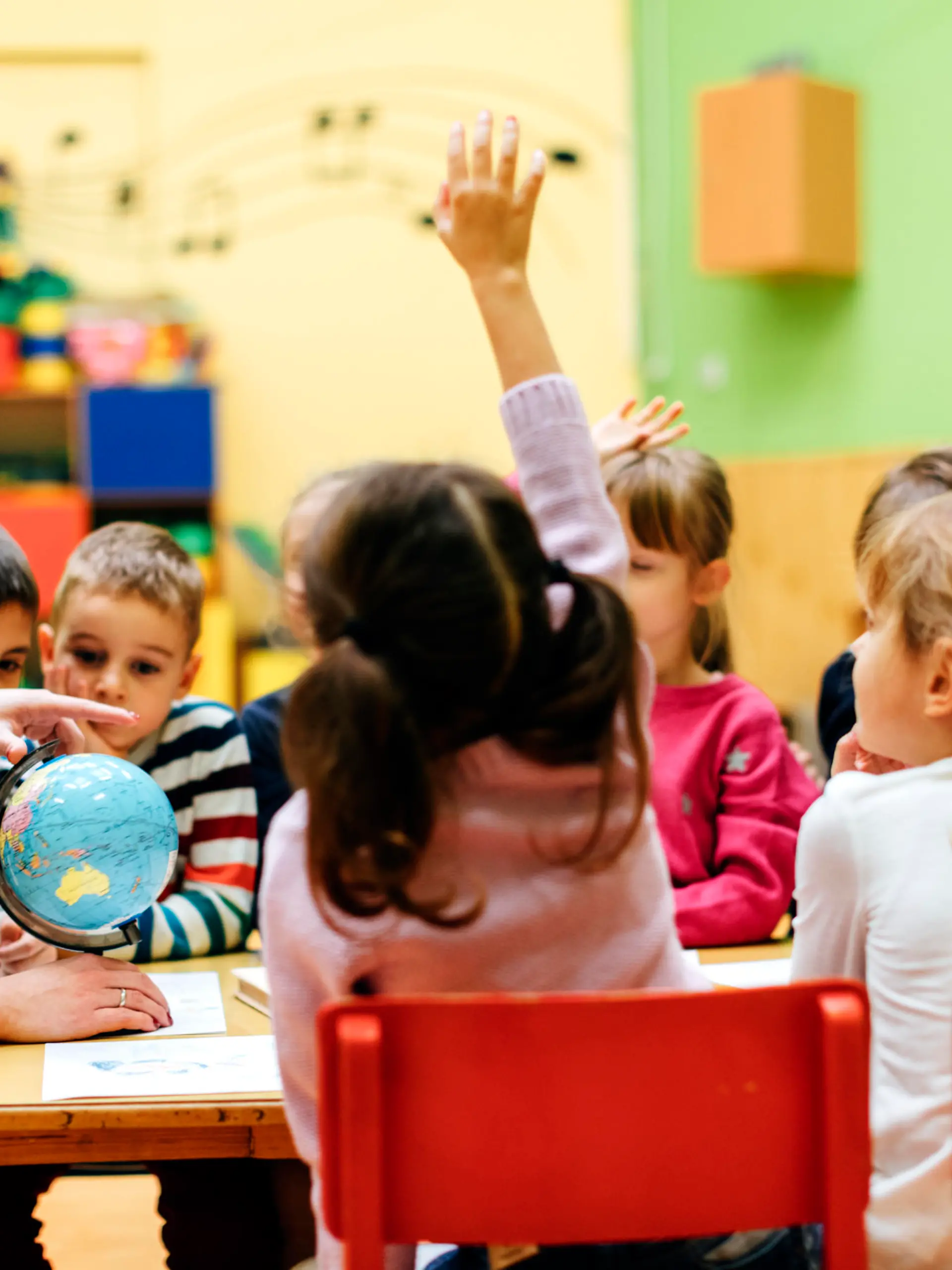 Preschool teacher teaching her children about geography. Using globe and asking the questions. Children  answering the questions. They are sitting by the table. Models in this shot are part of real kindergarten group and their teacher.