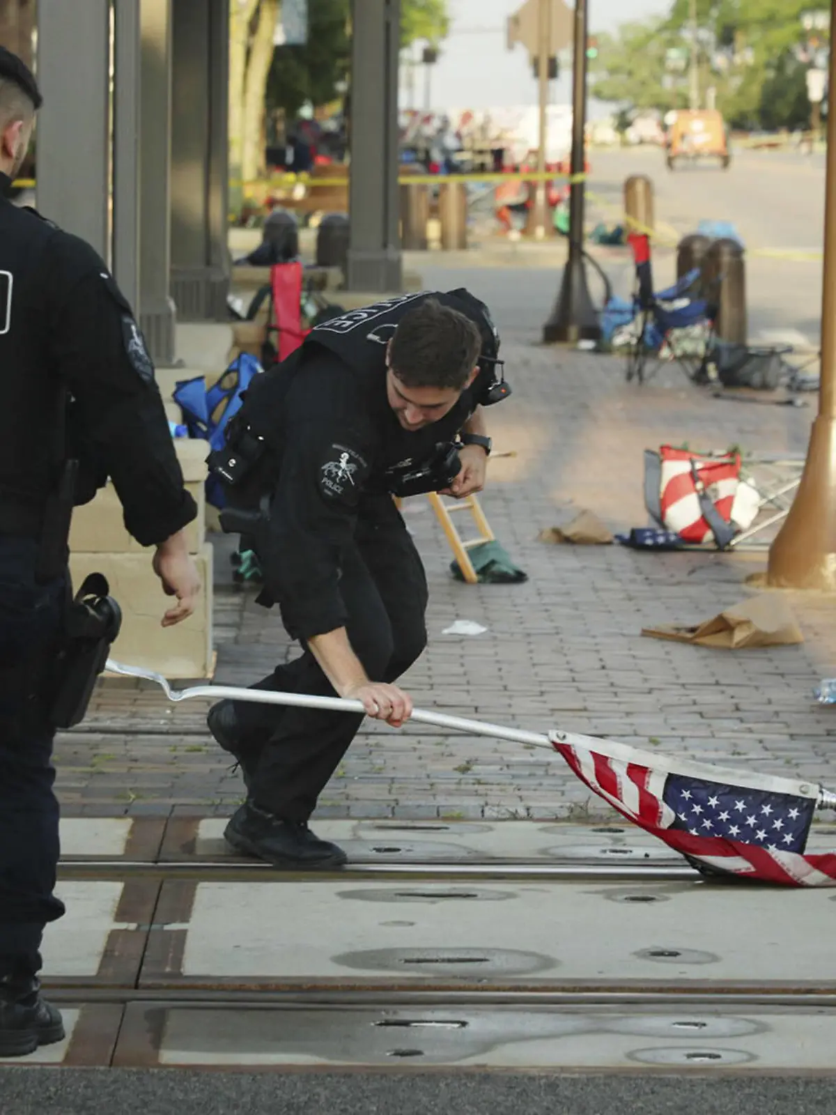  July 5, 2022, Chicago, Illinois, USA: A police officer picks up a water-logged American flag, Tuesday, left behind after Monday s mass shooting in Highland Park, Illinois. Six people were killed and dozens injured in the shooting on Monday. Chicago USA - ZUMAm67_ 20220705_zaf_m67_016 Copyright: xStaceyxWescottx