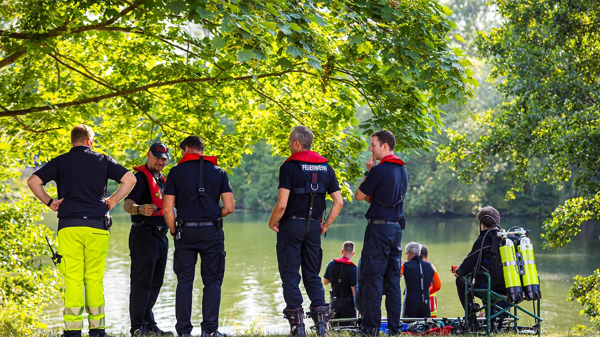 30.06.2022, Niedersachsen, Hannover: Einsatzkräfte der Deutschen Lebens-Rettungs-Gesellschaft (DLRG), vom Rettungsdienst und der Feuerwehr stehen am Dreiecksteich. In dem Baggersee ist ein Mann ertrunken. Foto: Moritz Frankenberg/dpa +++ dpa-Bildfunk +++