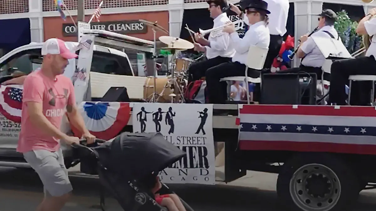 In this still image from video, a man runs for cover with a child in a stroller after gunfire was heard at the Fourth of July parade in the Chicago suburb of Highland Park, Monday morning, July 4, 2022. (Lynn Sweet/Chicago Sun-Times via AP)