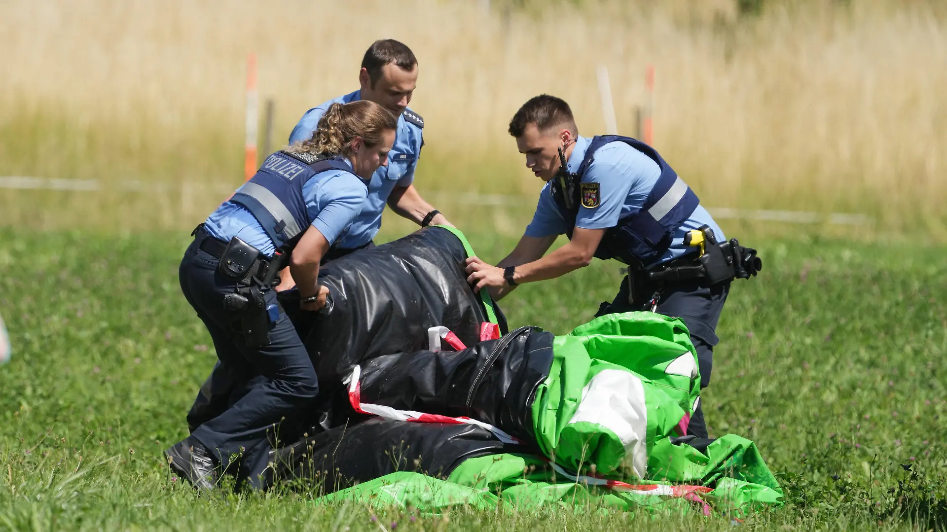 03.07.2022, Rheinland-Pfalz, Gondershausen: Polizeibeamte transportieren die Hülle einer Hüpfburg ab. Das Spielgerät war bei einem Fest auf dem Sportplatz von Gondershausen von einer Windböe erfasst und mindestens vier Meter in die Höhe gehoben worden. Vier Kinder wurden verletzt. Foto: Thomas Frey/dpa +++ dpa-Bildfunk +++