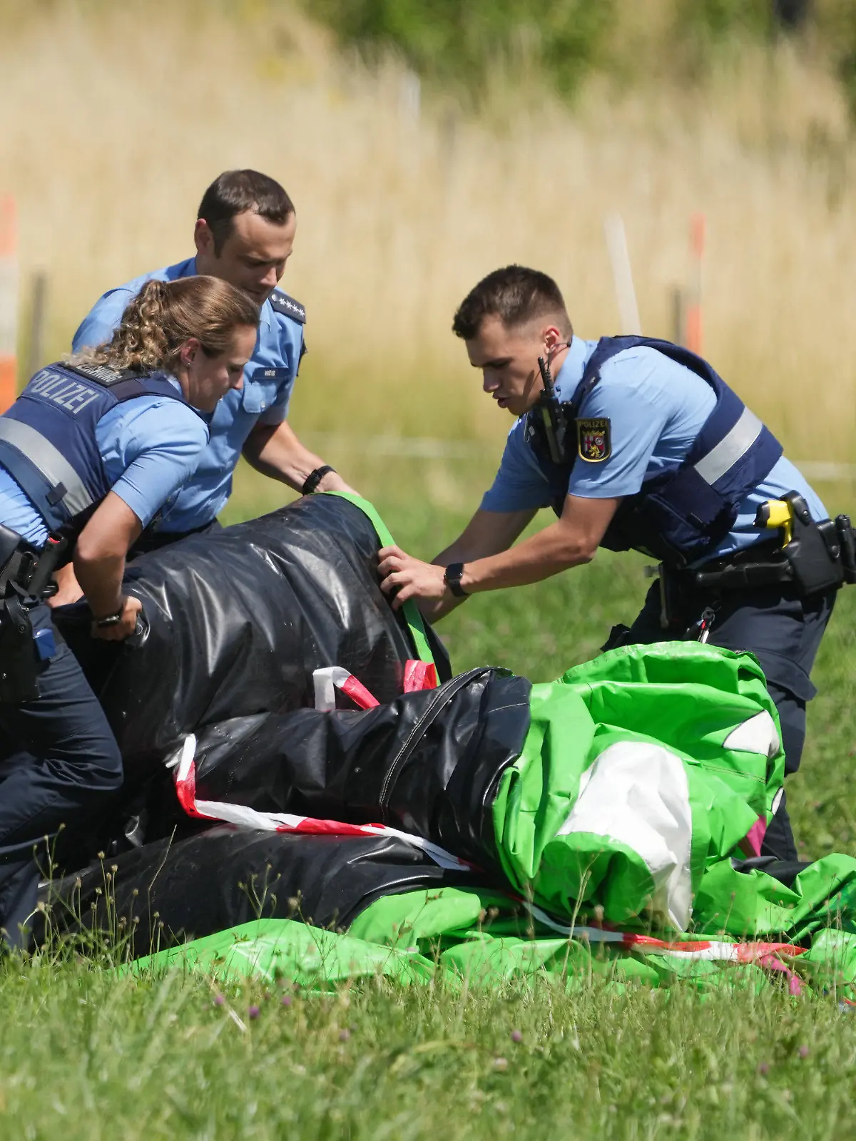 03.07.2022, Rheinland-Pfalz, Gondershausen: Polizeibeamte transportieren die Hülle einer Hüpfburg ab. Das Spielgerät war bei einem Fest auf dem Sportplatz von Gondershausen von einer Windböe erfasst und mindestens vier Meter in die Höhe gehoben worden. Vier Kinder wurden verletzt. Foto: Thomas Frey/dpa +++ dpa-Bildfunk +++
