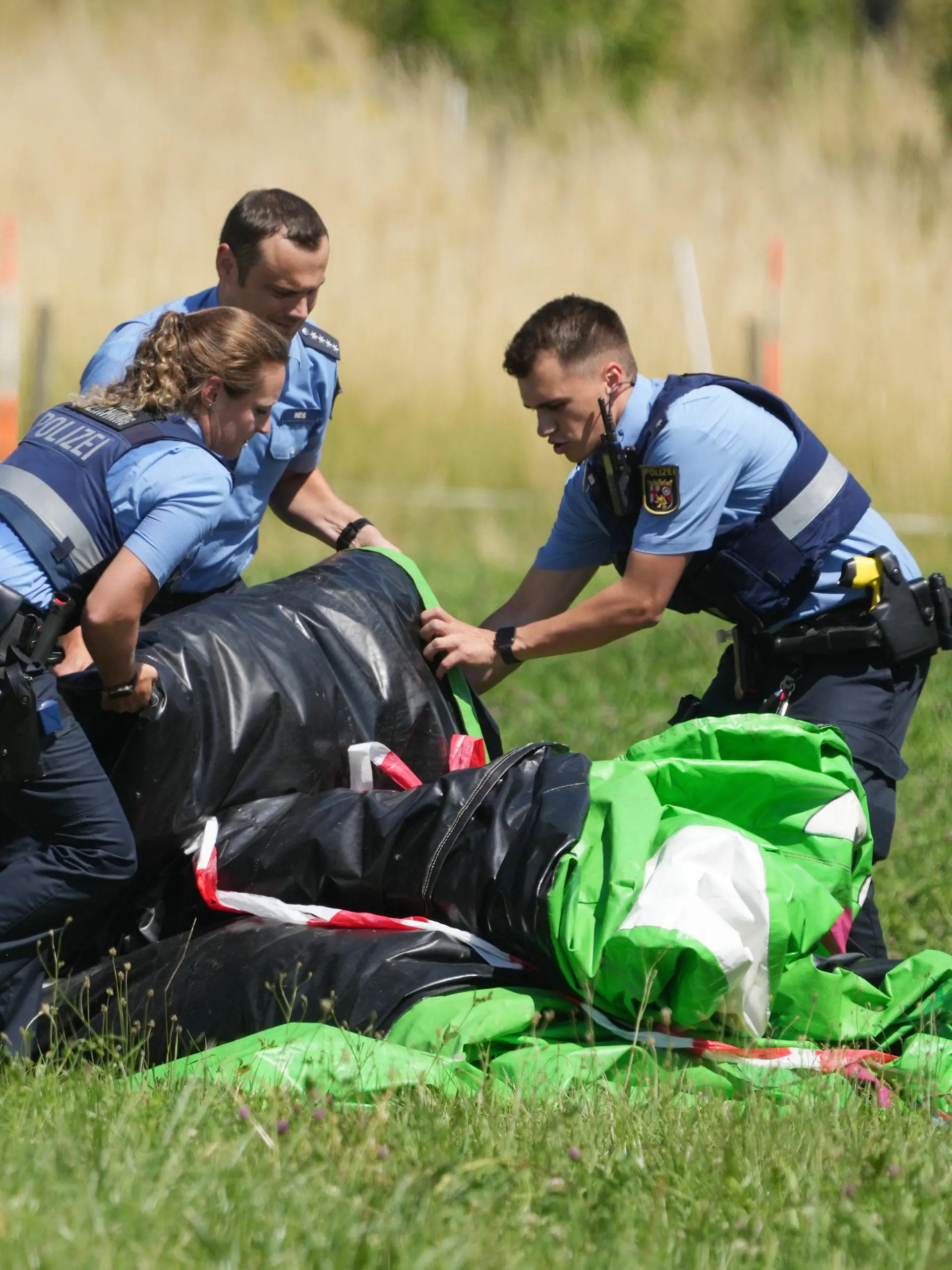 03.07.2022, Rheinland-Pfalz, Gondershausen: Polizeibeamte transportieren die Hülle einer Hüpfburg ab. Das Spielgerät war bei einem Fest auf dem Sportplatz von Gondershausen von einer Windböe erfasst und mindestens vier Meter in die Höhe gehoben worden. Vier Kinder wurden verletzt. Foto: Thomas Frey/dpa +++ dpa-Bildfunk +++