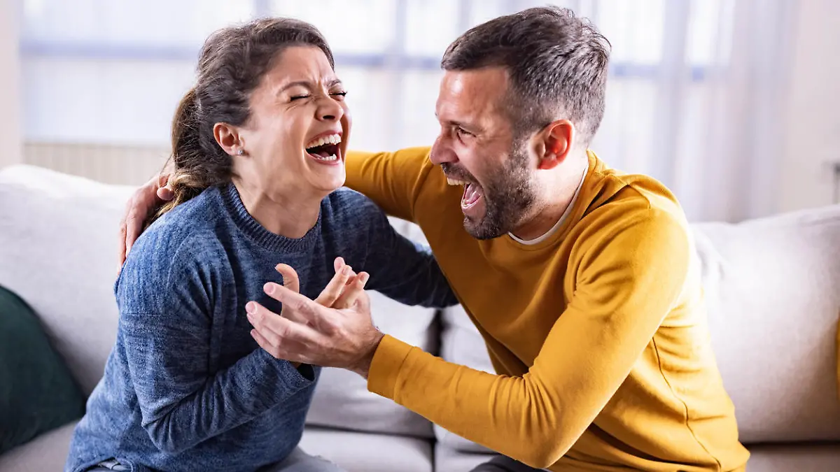 Embraced couple having fun while laughing hard at home.