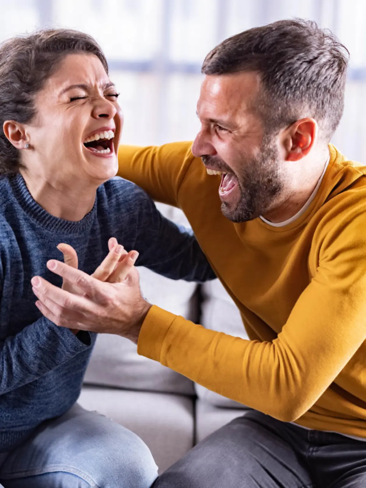 Embraced couple having fun while laughing hard at home.