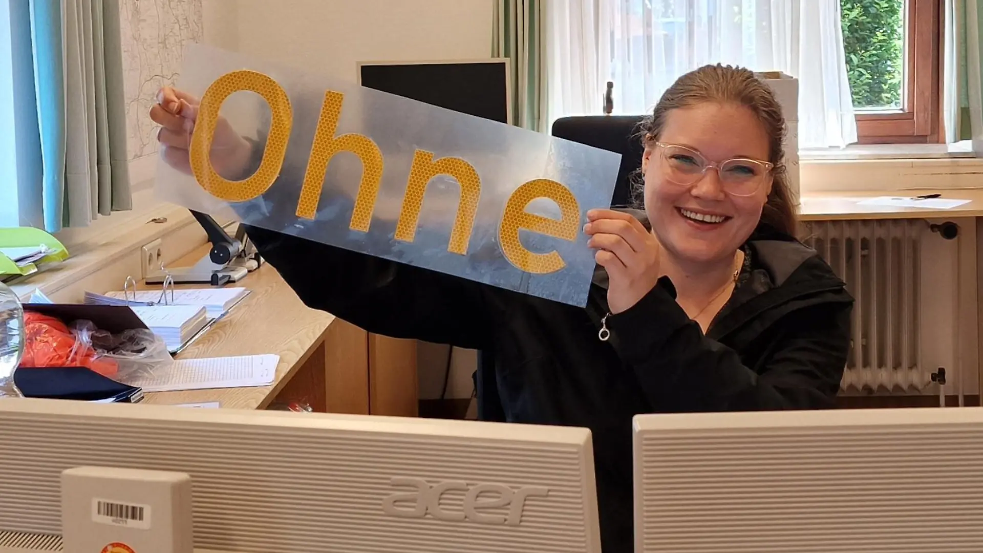 Lisa Brüning von der Straßenmeisterei Nordhorn hält den Schriftzug hoch, der auf dem Ortshinweisschild nachträglich aufgebracht wurde.