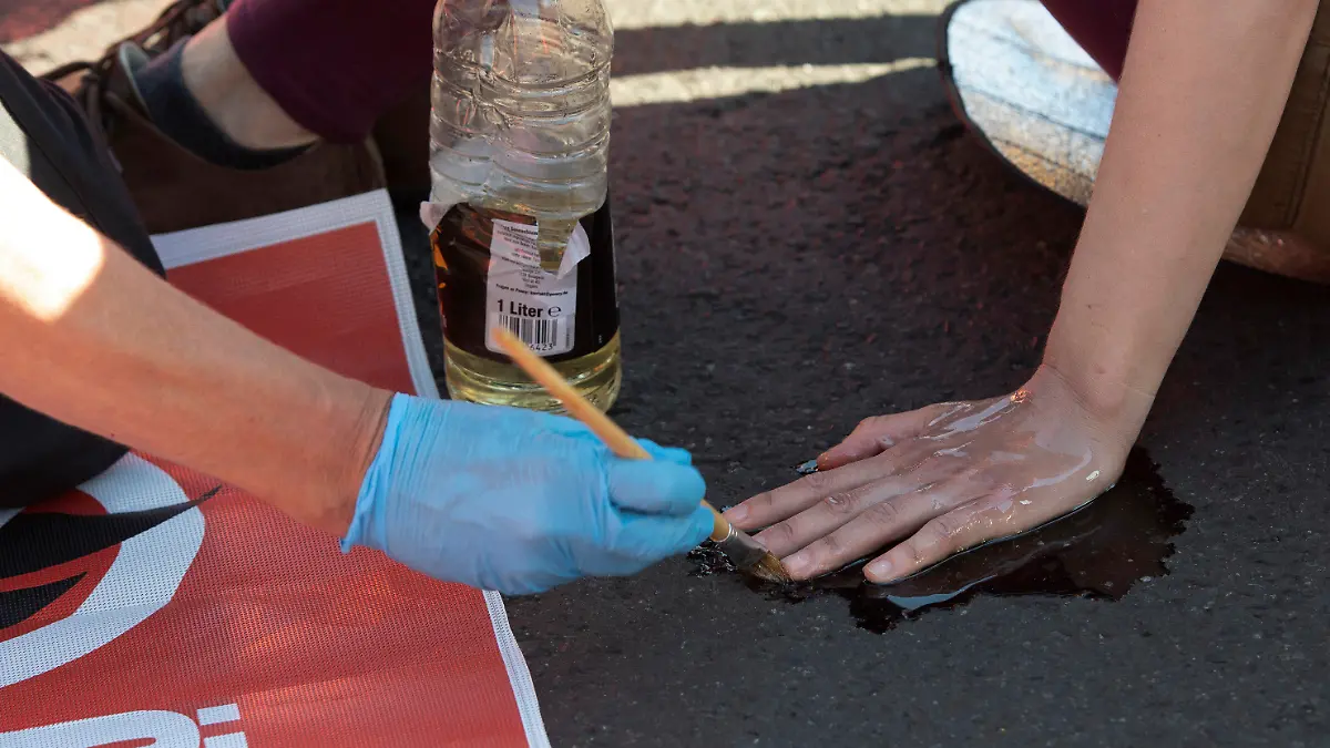 23.06.2022, Berlin: Ein Polizeibeamter löst mit Sonnenblumenöl die festgeklebte Hand eines Klimaschutz-Demonstranten der Gruppe "Letzte Generation" vom Asphalt auf der Kreuzung am Frankfurter Tor. Allen Zufahrten sowie den Kreuzungsbereich hatten die Aktivisten blockiert, zahlreiche von ihnen klebten sich auf den Asphalt fest. Es kam zu erheblichen Verkehrsstörungen. Foto: Paul Zinken/dpa +++ dpa-Bildfunk +++