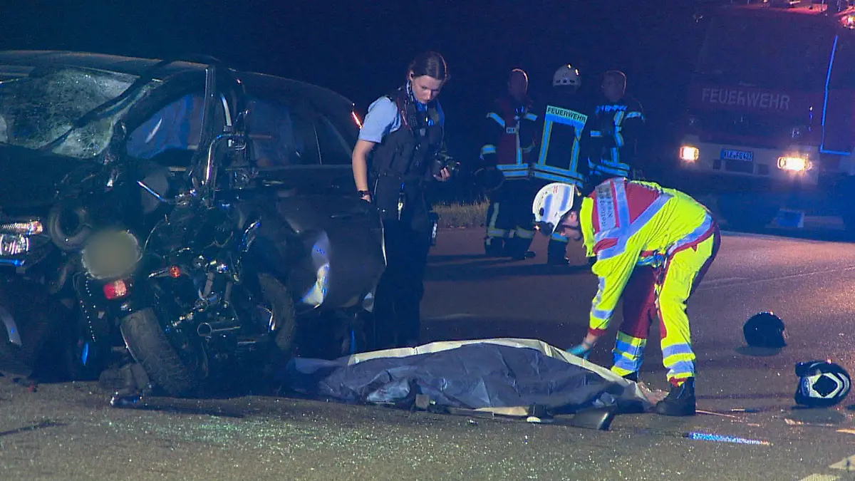 30.06.2022, Nordrhein-Westfalen, Goch: Polizei und Rettungsdienst arbeiten an der Unfallstelle, nachdem ein Auto mit einem Motorrad zusammengestoßen ist, wobei zwei Menschen ums Leben gekommen sind. Zwei weitere sind schwer verletzt, wie die Polizei am Donnerstag mitteilt. Am späten Mittwochabend bog eine 71-jährige Pkw-Fahrerin in Goch im Landkreis Kleve von einem Privatgrundstück nach links auf die B504 und kollidierte dabei mit dem Motorrad. Der 59-jährige Motorradfahrer sowie seine 62-jährige Beifahrerin überlebten den Zusammenstoß nicht. Foto: Guido Schulmann/tv-niederrhein/dpa +++ dpa-Bildfunk +++