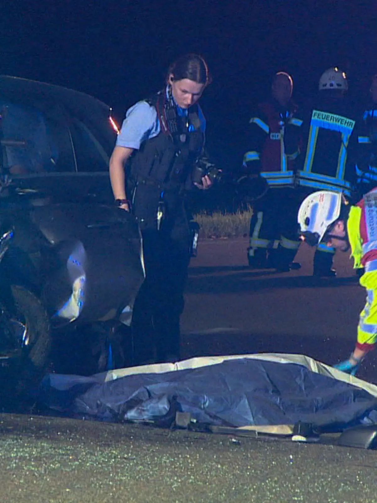 30.06.2022, Nordrhein-Westfalen, Goch: Polizei und Rettungsdienst arbeiten an der Unfallstelle, nachdem ein Auto mit einem Motorrad zusammengestoßen ist, wobei zwei Menschen ums Leben gekommen sind. Zwei weitere sind schwer verletzt, wie die Polizei am Donnerstag mitteilt. Am späten Mittwochabend bog eine 71-jährige Pkw-Fahrerin in Goch im Landkreis Kleve von einem Privatgrundstück nach links auf die B504 und kollidierte dabei mit dem Motorrad. Der 59-jährige Motorradfahrer sowie seine 62-jährige Beifahrerin überlebten den Zusammenstoß nicht. Foto: Guido Schulmann/tv-niederrhein/dpa +++ dpa-Bildfunk +++