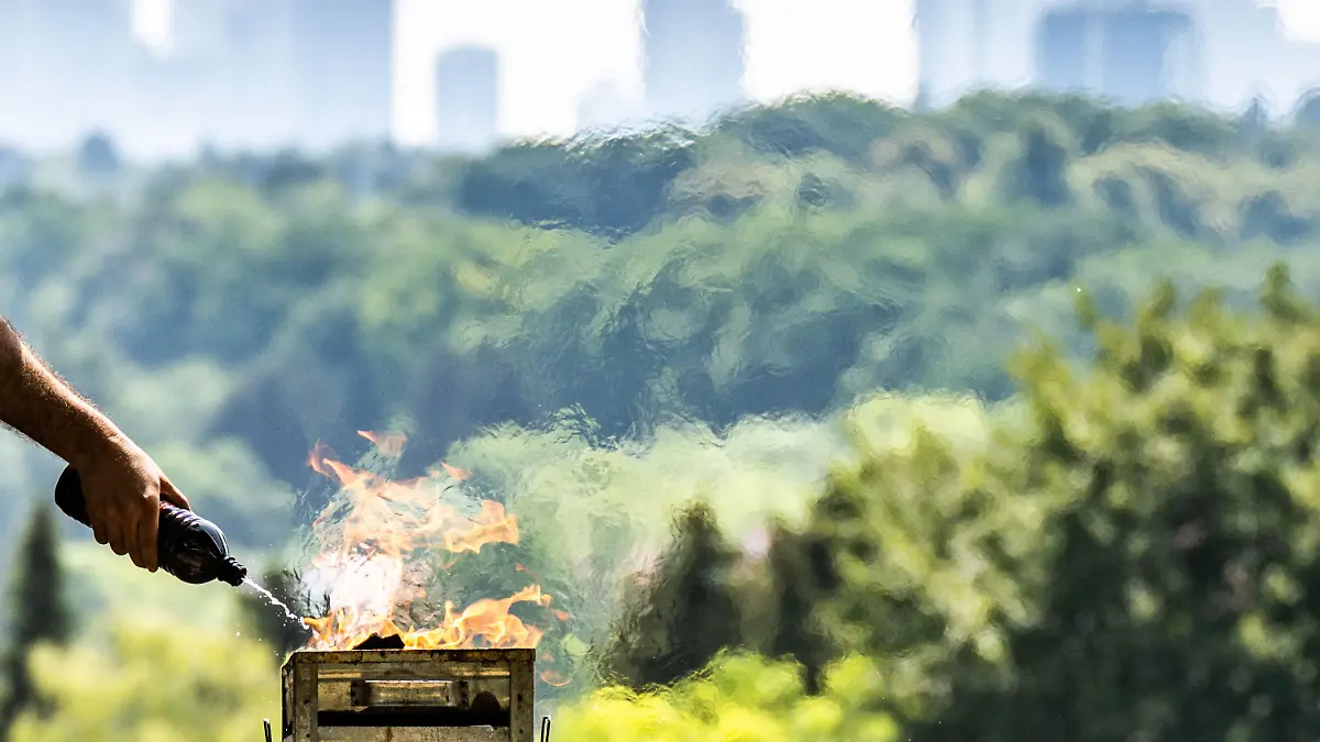 19.06.2022, Hessen, Frankfurt/Main: Ein Mann spritzt Brennspritus aus einer Flasche, um in der Nachmittagshitze das Feuer in einem Grill auf dem Lohrberg mit Blick auf die Skjyline der Stadt anzuheizen. Im Süden Hessens wurden bis zu 37 Grad Hitze gemeldet und wegen der Trockenheit mangels Niederschlägen besteht in Teilen des Landes weiter hohe Waldbrandgefahr. Foto: Frank Rumpenhorst/dpa +++ dpa-Bildfunk +++