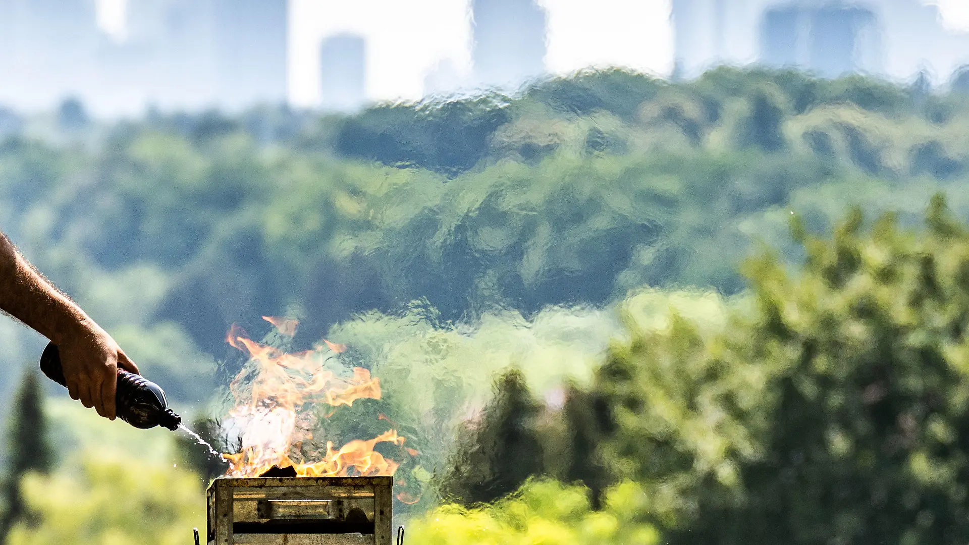 19.06.2022, Hessen, Frankfurt/Main: Ein Mann spritzt Brennspritus aus einer Flasche, um in der Nachmittagshitze das Feuer in einem Grill auf dem Lohrberg mit Blick auf die Skjyline der Stadt anzuheizen. Im Süden Hessens wurden bis zu 37 Grad Hitze gemeldet und wegen der Trockenheit mangels Niederschlägen besteht in Teilen des Landes weiter hohe Waldbrandgefahr. Foto: Frank Rumpenhorst/dpa +++ dpa-Bildfunk +++