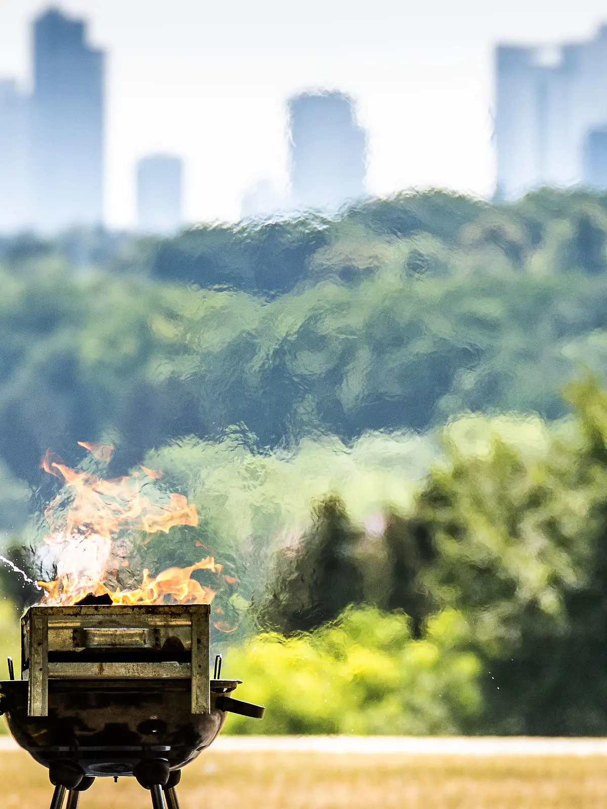 19.06.2022, Hessen, Frankfurt/Main: Ein Mann spritzt Brennspritus aus einer Flasche, um in der Nachmittagshitze das Feuer in einem Grill auf dem Lohrberg mit Blick auf die Skjyline der Stadt anzuheizen. Im Süden Hessens wurden bis zu 37 Grad Hitze gemeldet und wegen der Trockenheit mangels Niederschlägen besteht in Teilen des Landes weiter hohe Waldbrandgefahr. Foto: Frank Rumpenhorst/dpa +++ dpa-Bildfunk +++