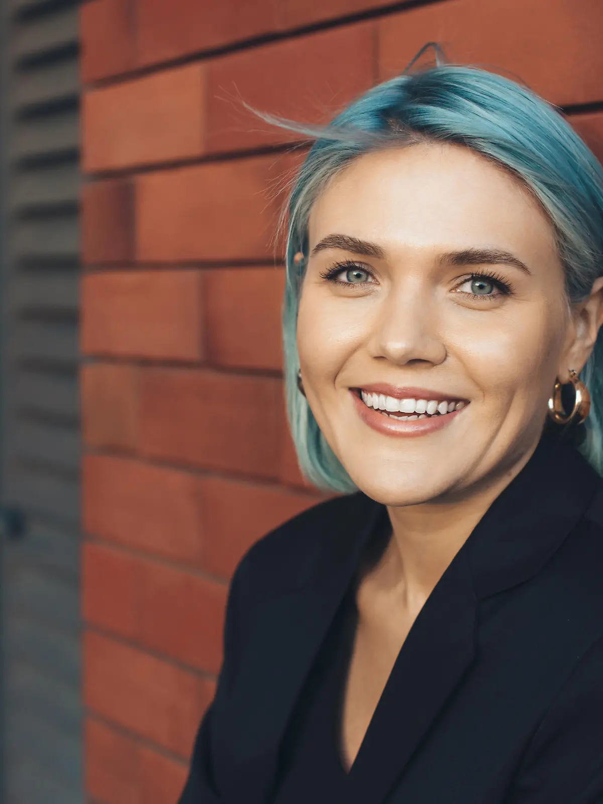 Frau mit blauen Haaren und blauen Augen lächelt in die Kamera.