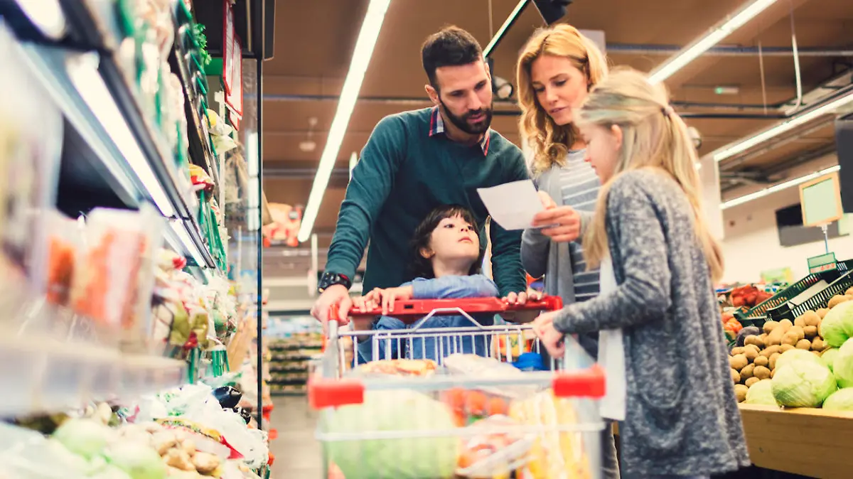 Cheerful family with two children shopping vegetables in supermarket. Holding shopping list and looking for groceries