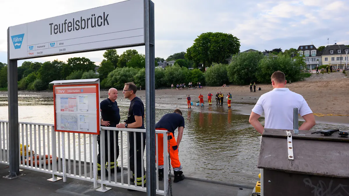 25.06.2022, Hamburg: Einsatzkräfte von Feuerwehr, DLRG und Polizei stehen während der Suche auf dem Anleger "Teufelsbrück" und am Ufer der Elbe. Ein 13-jähriger Nichtschwimmer ist am Samstagabend in Hamburg-Nienstedten in der Elbe untergegangen. Foto: Jonas Walzberg/dpa +++ dpa-Bildfunk +++