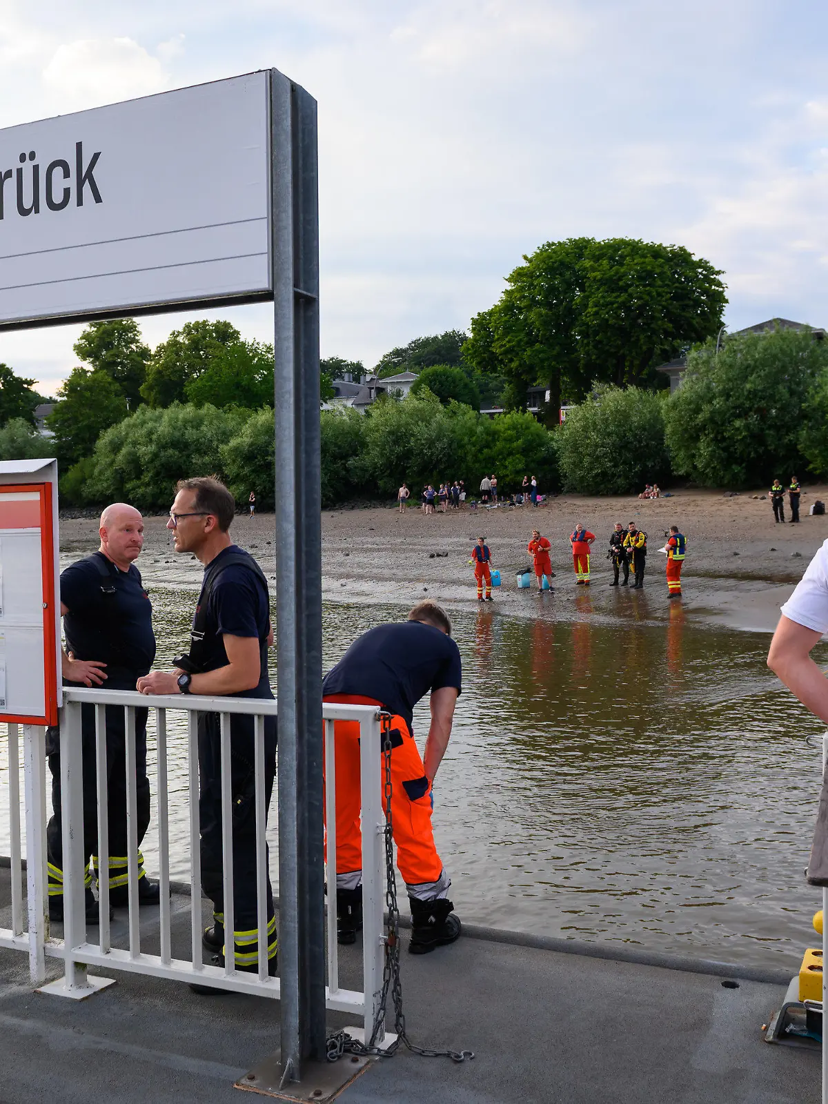 25.06.2022, Hamburg: Einsatzkräfte von Feuerwehr, DLRG und Polizei stehen während der Suche auf dem Anleger "Teufelsbrück" und am Ufer der Elbe. Ein 13-jähriger Nichtschwimmer ist am Samstagabend in Hamburg-Nienstedten in der Elbe untergegangen. Foto: Jonas Walzberg/dpa +++ dpa-Bildfunk +++