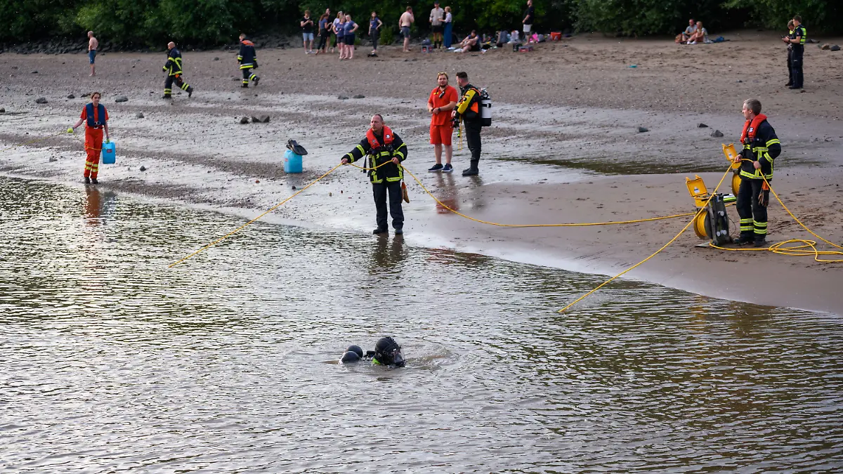 25.06.2022, Hamburg: Einsatzkräfte der Taucheinheiten von Feuerwehr und DLRG stehen am Ufer der Elbe und sichern ihre Kollegen im Wasser an gelben Leinen. Ein 13-jähriger Nichtschwimmer ist am Samstagabend in Hamburg-Nienstedten in der Elbe untergegangen. Foto: Jonas Walzberg/dpa +++ dpa-Bildfunk +++