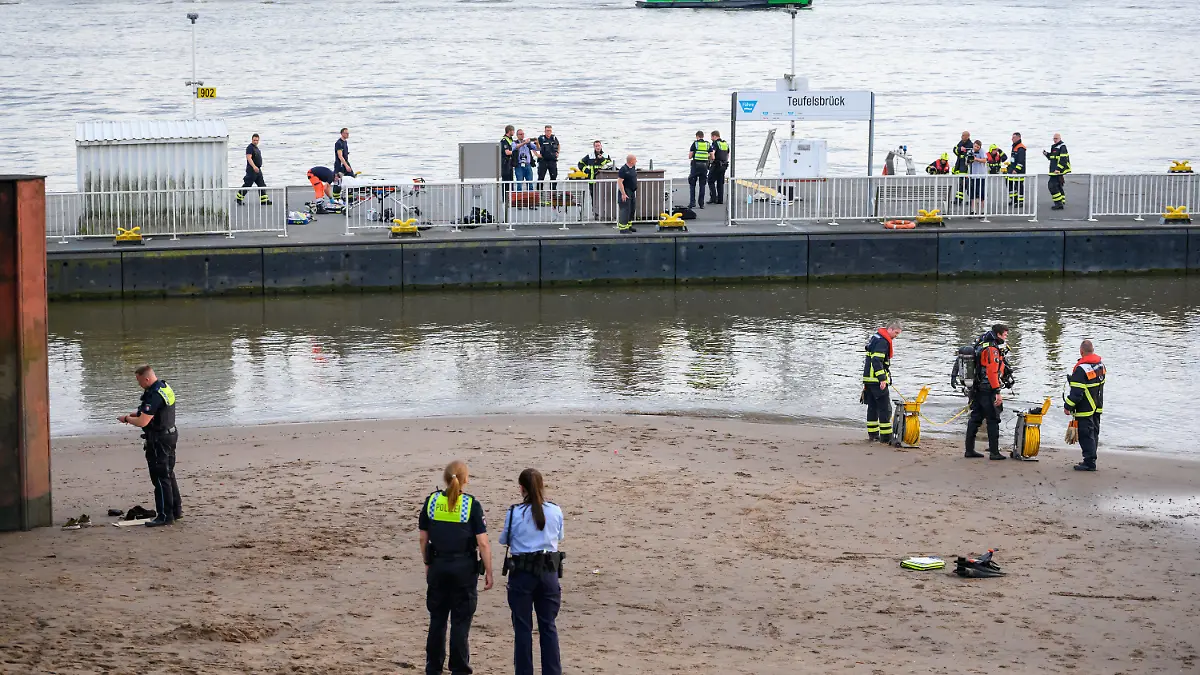 25.06.2022, Hamburg: Einsatzkräfte von Feuerwehr, DLRG und Polizei stehen während der Suche auf dem Anleger "Teufelsbrück" und am Ufer der Elbe. Ein 13-jähriger Nichtschwimmer ist am Samstagabend in Hamburg-Nienstedten in der Elbe untergegangen. Foto: Jonas Walzberg/dpa +++ dpa-Bildfunk +++