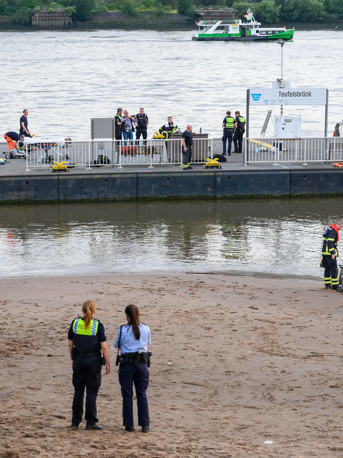 25.06.2022, Hamburg: Einsatzkräfte von Feuerwehr, DLRG und Polizei stehen während der Suche auf dem Anleger "Teufelsbrück" und am Ufer der Elbe. Ein 13-jähriger Nichtschwimmer ist am Samstagabend in Hamburg-Nienstedten in der Elbe untergegangen. Foto: Jonas Walzberg/dpa +++ dpa-Bildfunk +++