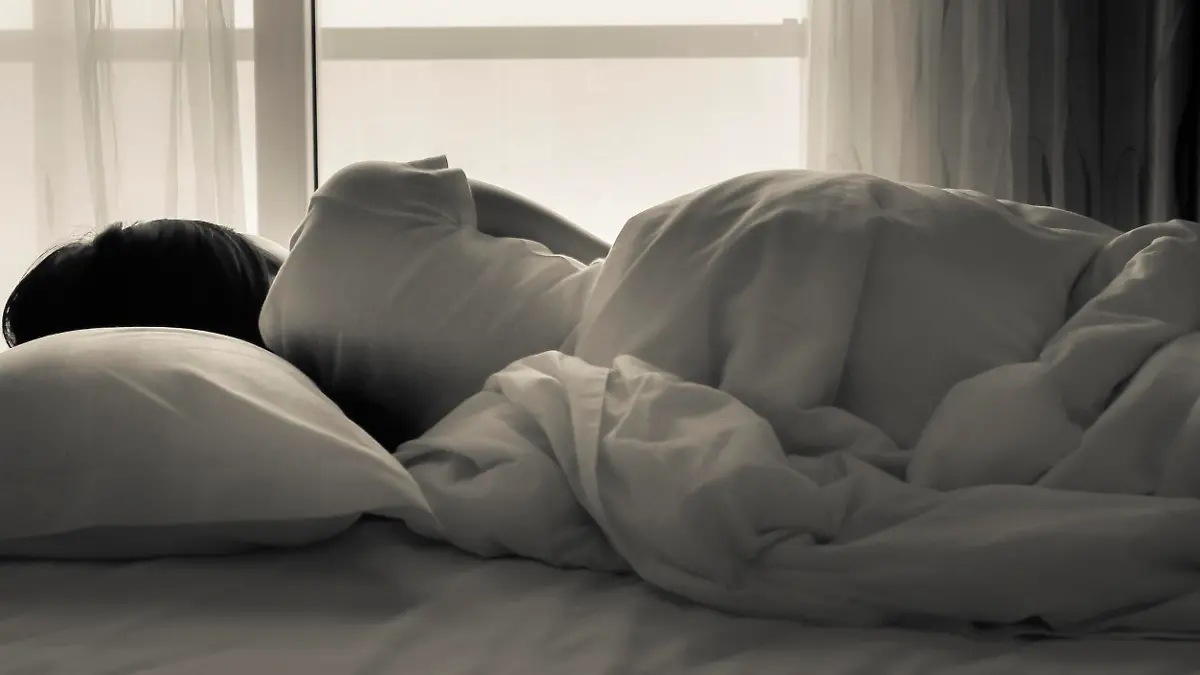 Young woman lying in bed, looking towards through the window - black and white photo.