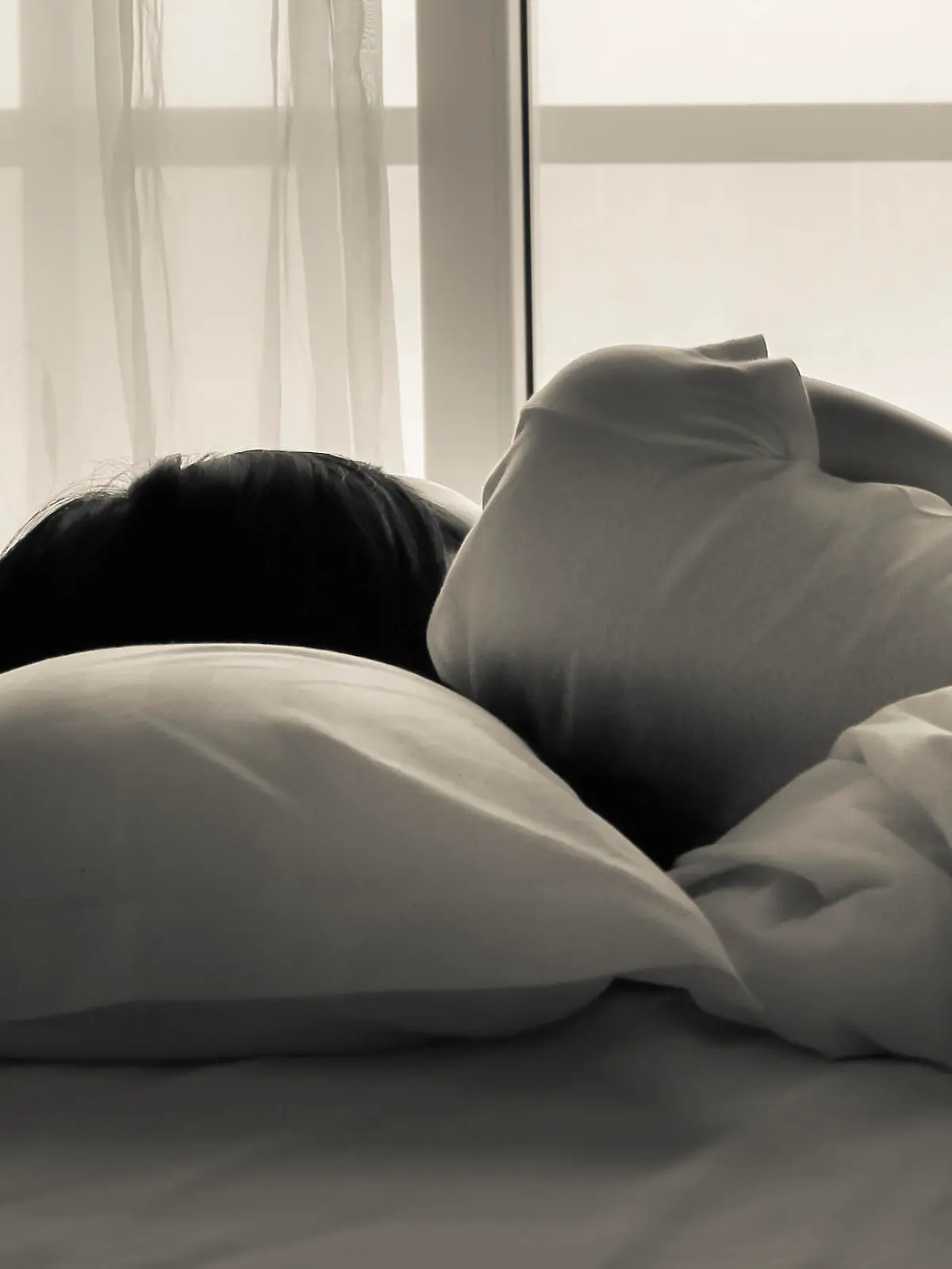 Young woman lying in bed, looking towards through the window - black and white photo.