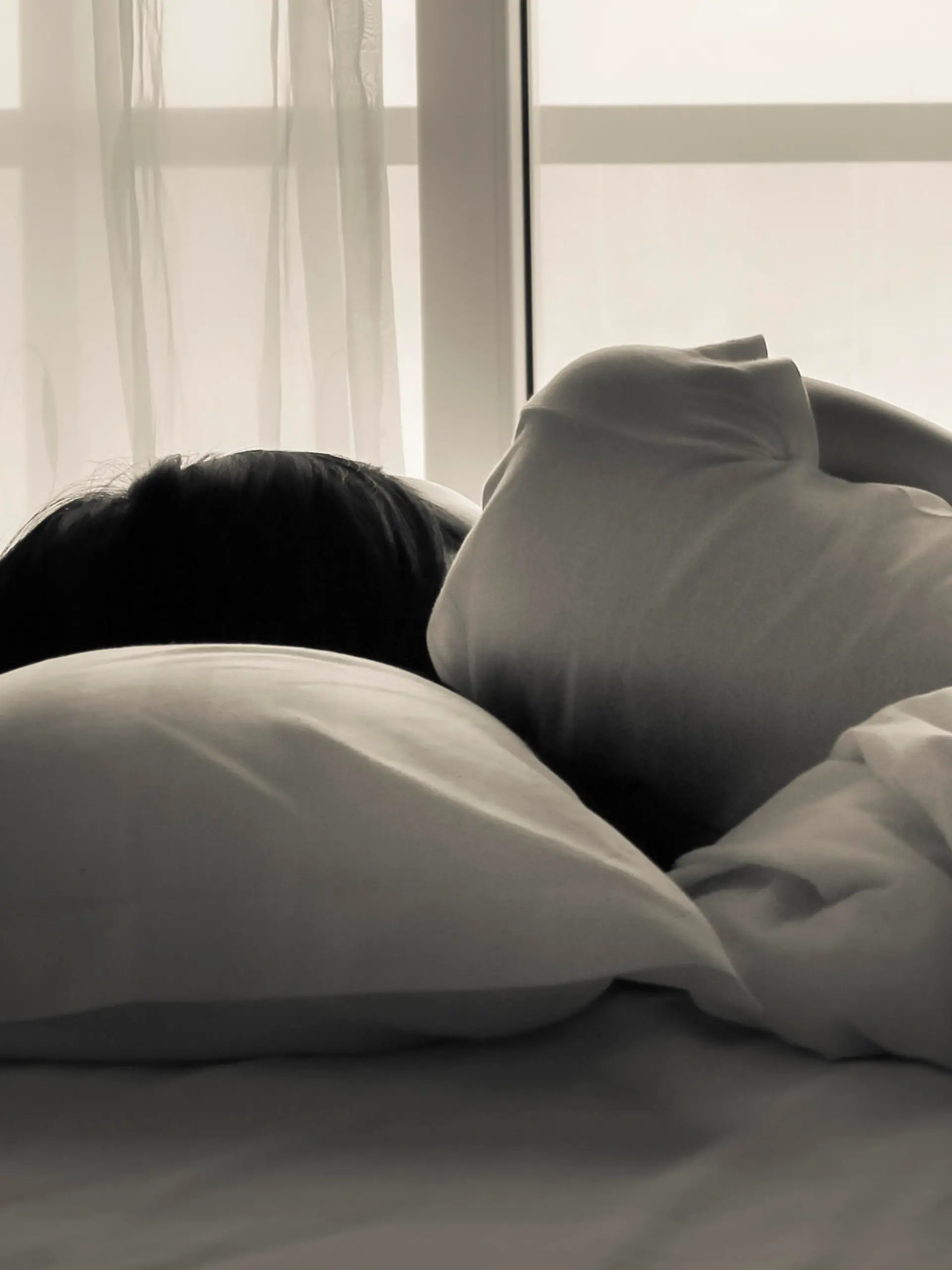 Young woman lying in bed, looking towards through the window - black and white photo.