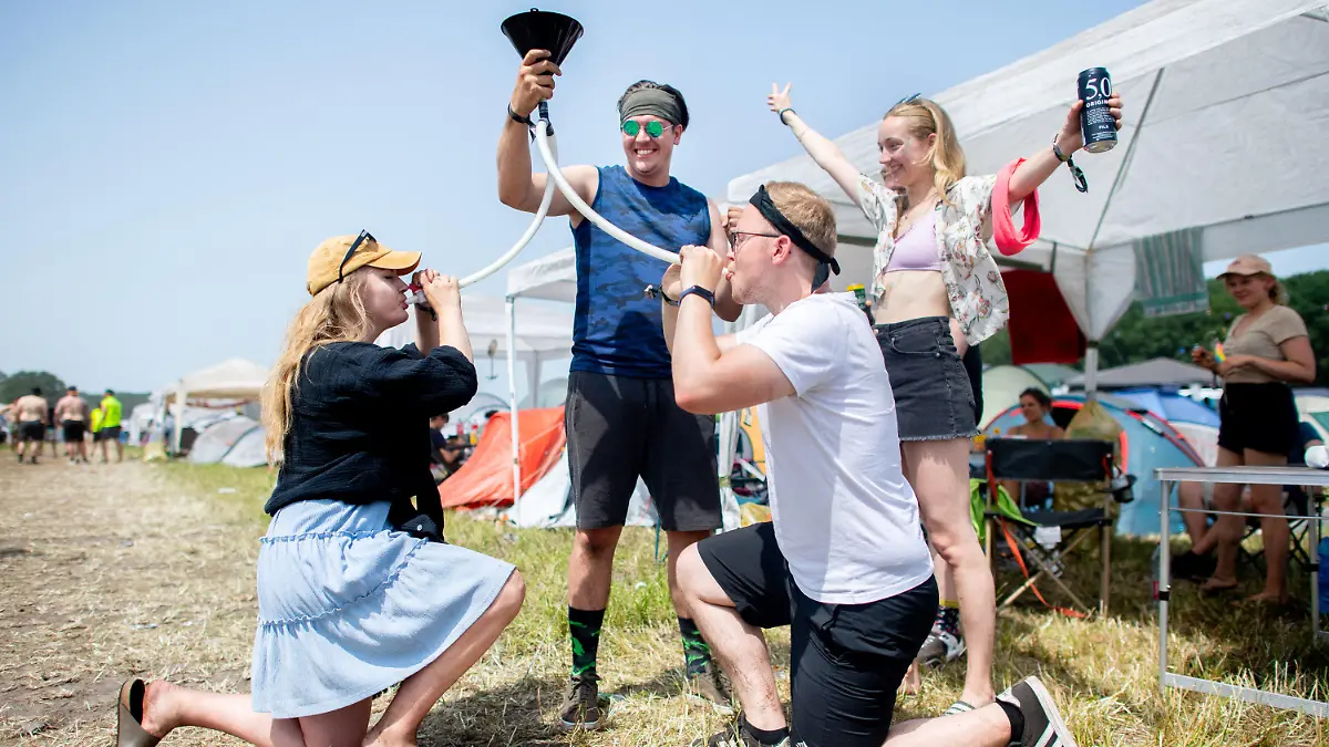 18.06.2022, Niedersachsen, Scheeßel: Annabell und Matthias (vorne) trinken auf dem Zeltplatz des Hurricane Festivals Bier aus einem Trichter, während Matthias den Trichter hält und Hannah jubelt. Das Open-Air-Festival mit rund 78.000 Besuchern pro Tag findet vom 17. bis zum 19. Juni statt. Foto: Hauke-Christian Dittrich/dpa +++ dpa-Bildfunk +++