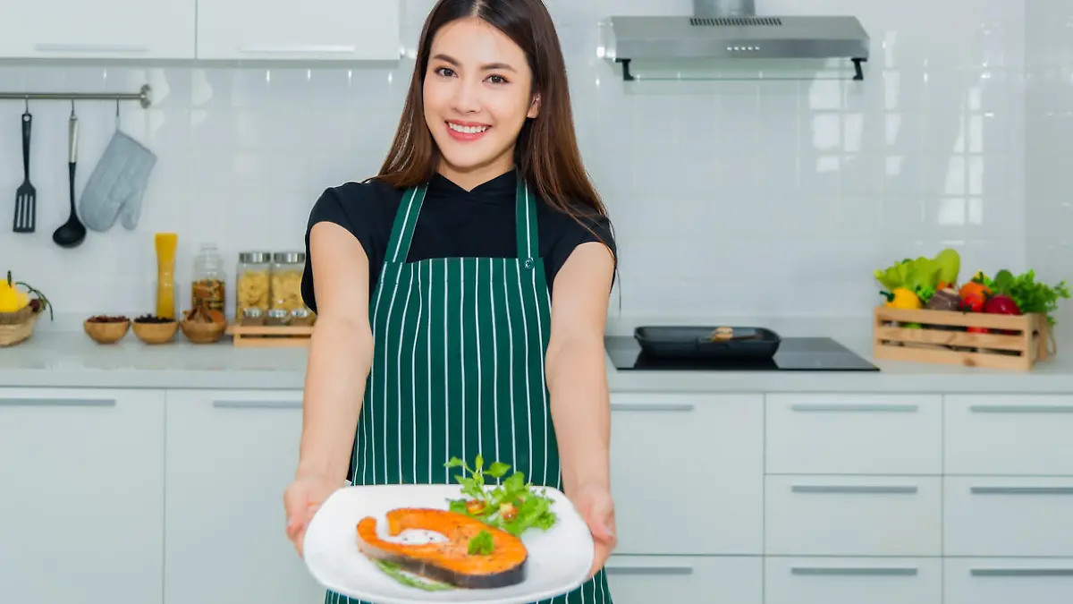Beautiful asian woman standing smiling holding dish salmon steak a health breakfast with happiness in the kitchen at home. Lifestyle and healthy concept.