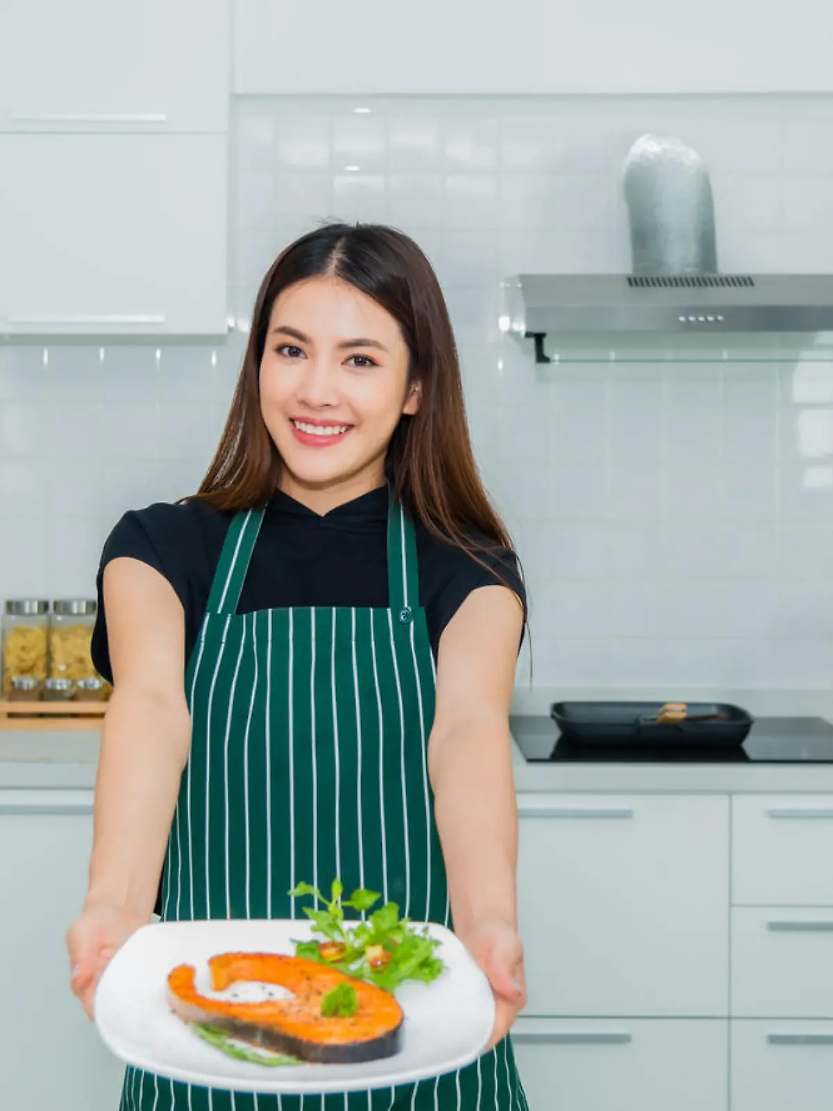 Beautiful asian woman standing smiling holding dish salmon steak a health breakfast with happiness in the kitchen at home. Lifestyle and healthy concept.