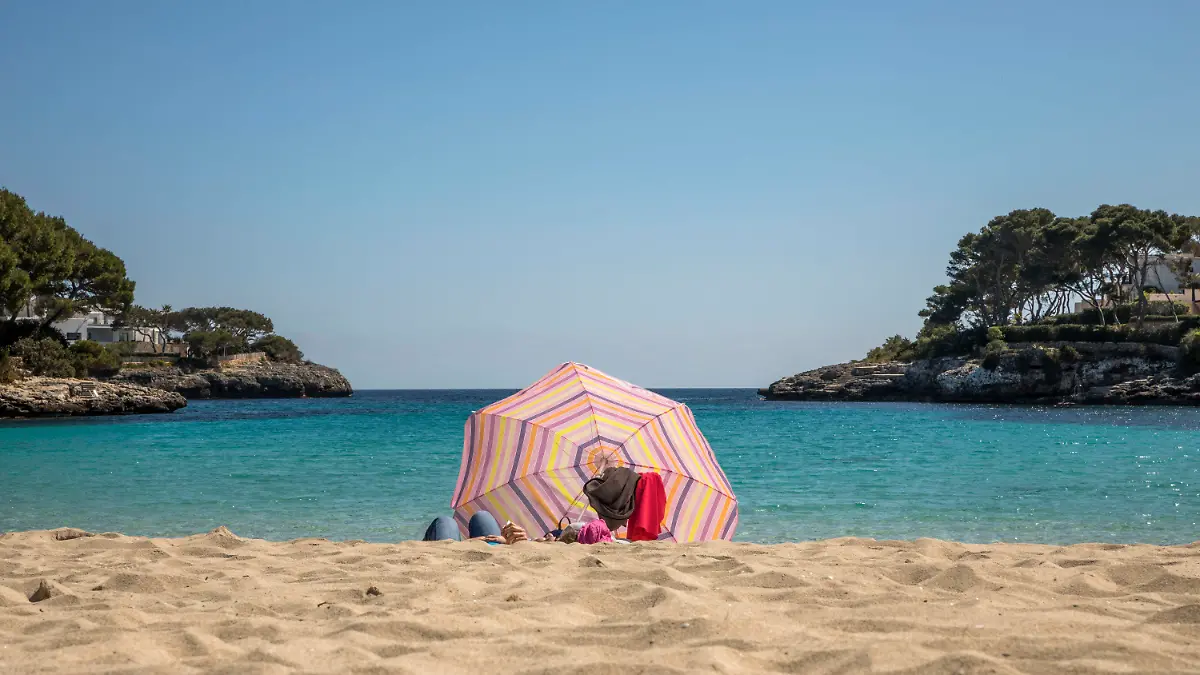 dpatopbilder - 25.03.2021, Spanien, Cala D'or: Zwei Personen liegen unter einem Sonnenschirm an einem Strand auf Mallorca. Angesichts der Corona-Pandemie sollen sich Flugpassagiere vor dem Start nach Deutschland künftig generell testen lassen müssen - und zwar ab diesem Sonntag um 0.00 Uhr. Foto: John-Patrick Morarescu/ZUMA Wire/dpa +++ dpa-Bildfunk +++